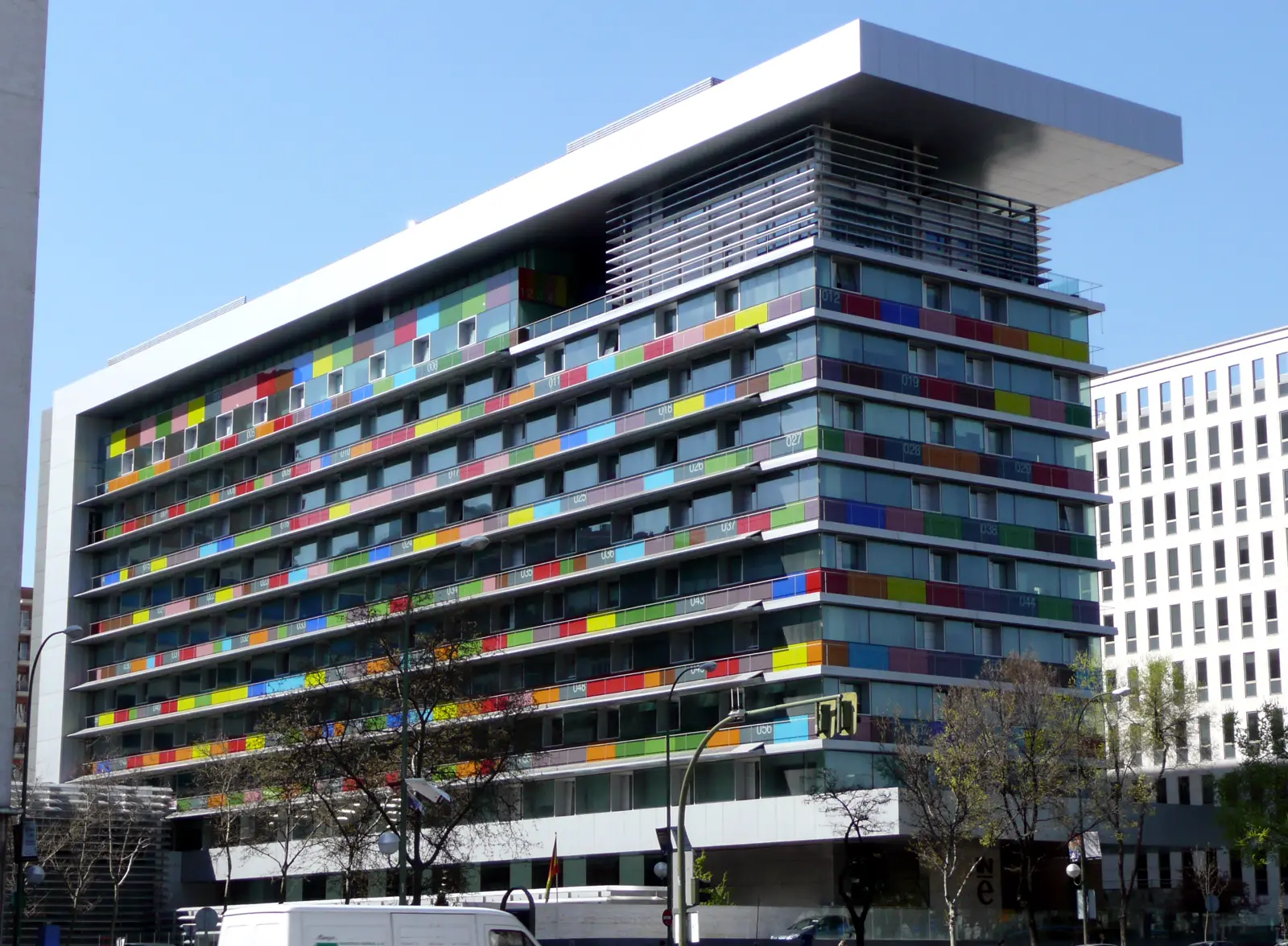 Fachada del edificio del Instituto Nacional de Estadística en Madrid, con paneles de colores entre las ventanas y una gran visera blanca en la azotea