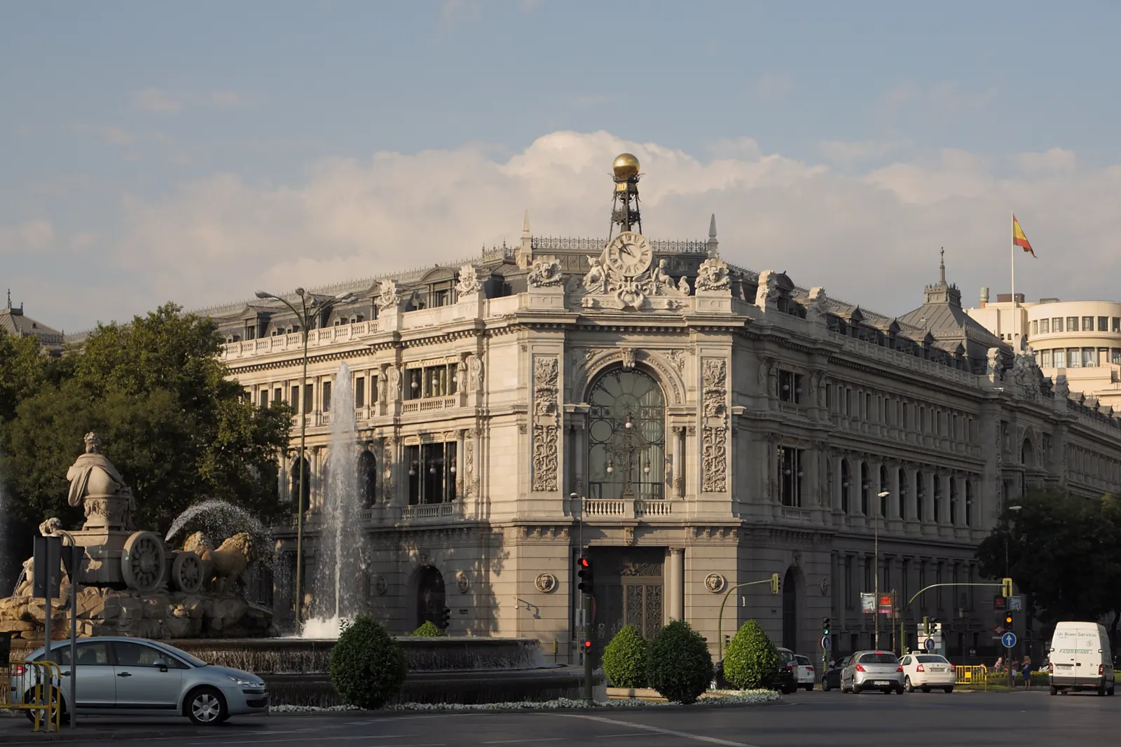 Fachada del edificio del Banco de España en Madrid, de piedra clara y con un reloj y una esfera dorada en la esquina, vista desde la plaza de Cibeles con la fuente en primer término.
