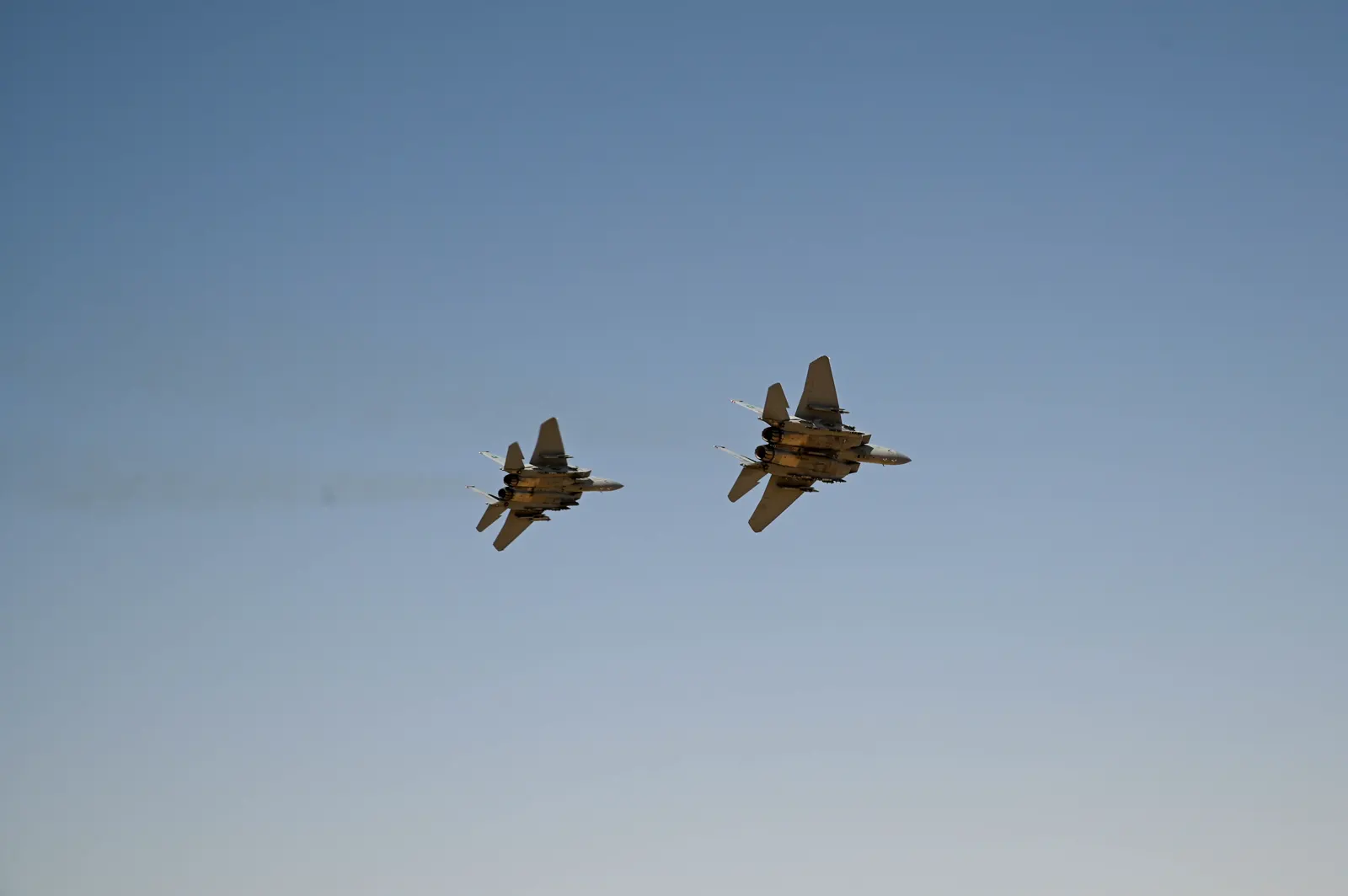 Dos cazas F-15 de la Fuerza Aérea de Arabia Saudí vuelan en formación sobre un cielo despejado, vistos desde tierra.