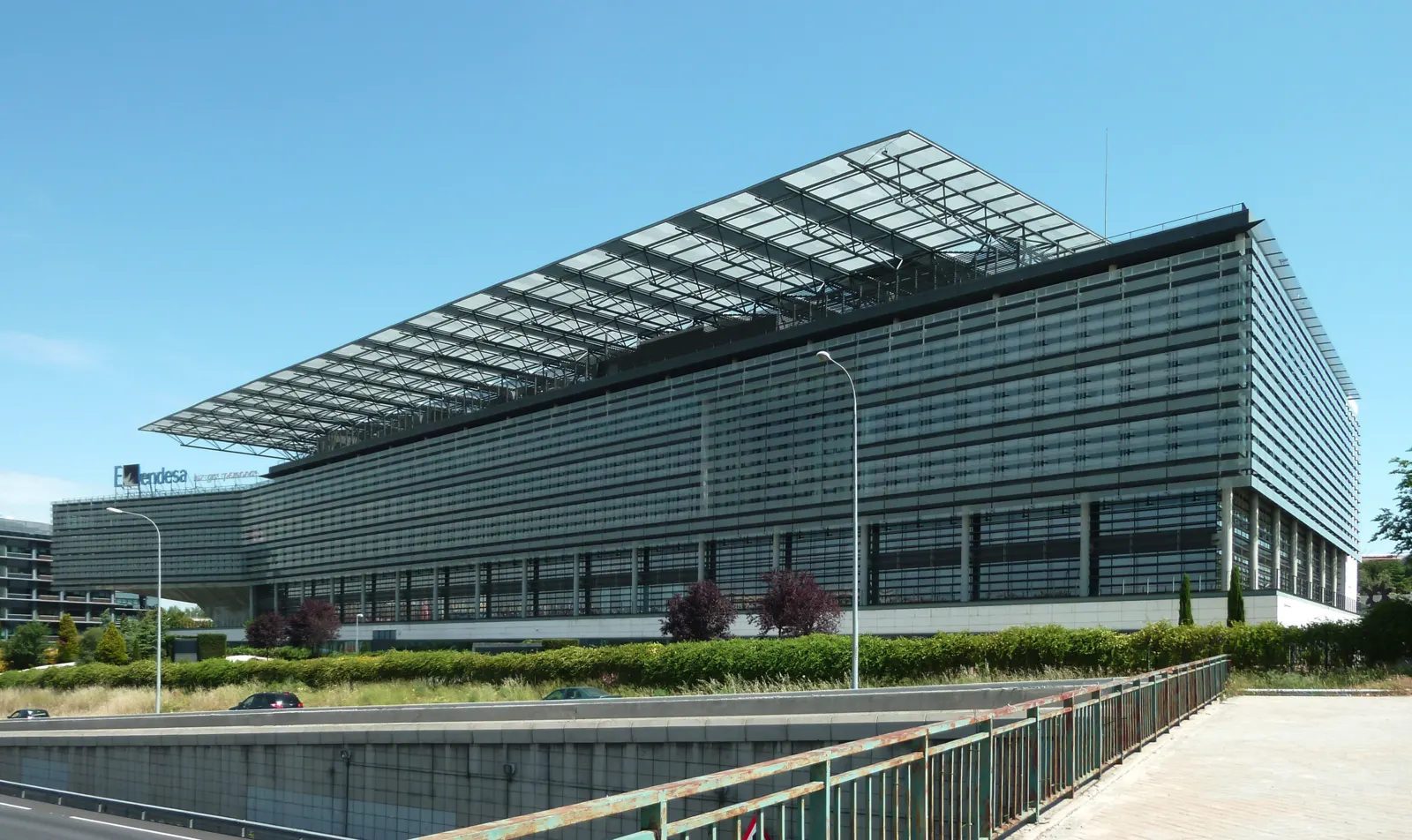 Fachada acristalada del edificio de la sede de Endesa en Madrid, con el logotipo de la compañía sobre la entrada y jardines delante