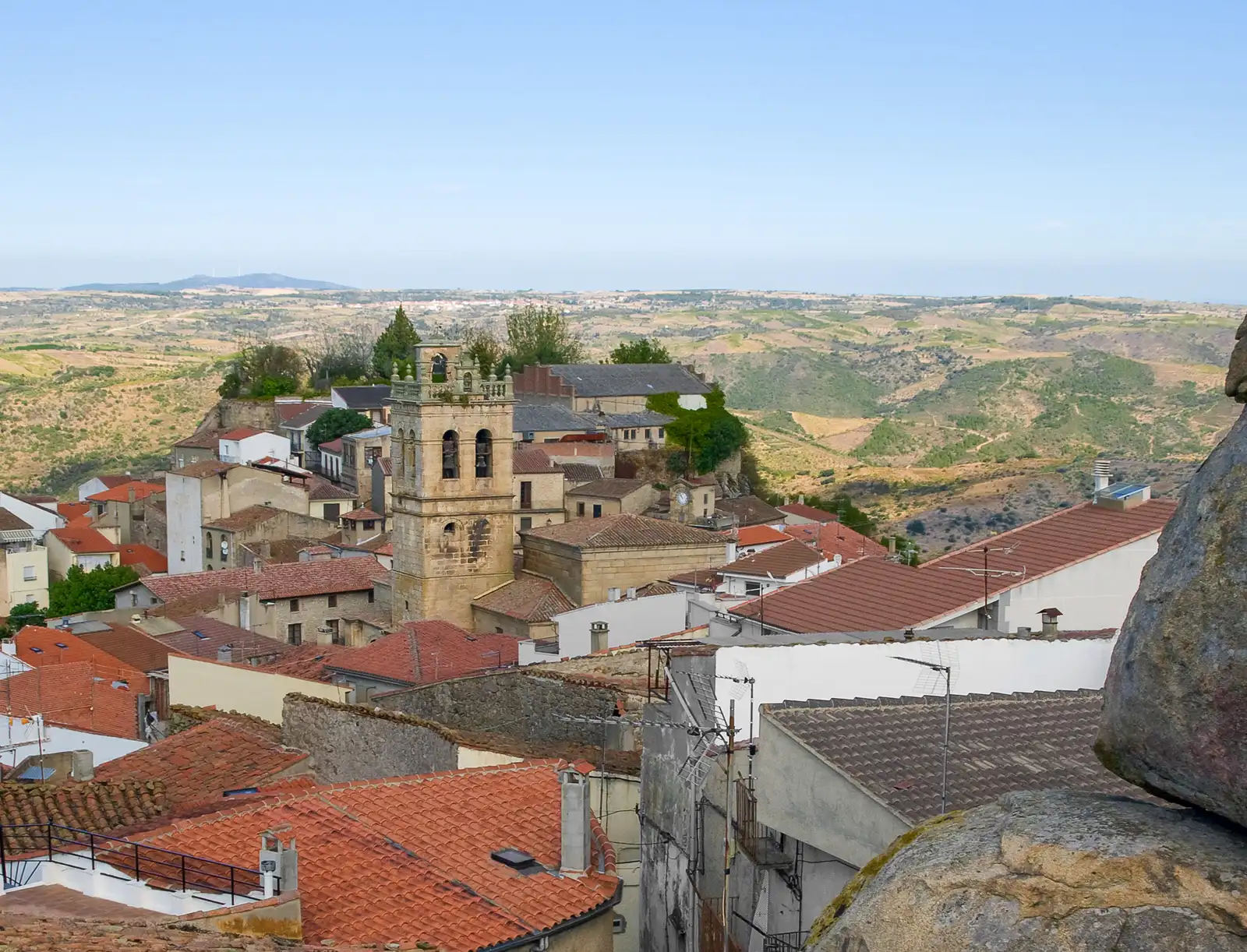 Vista de los tejados de Fermoselle (Zamora) con la torre de la iglesia en el centro y, al fondo, el paisaje de laderas de los Arribes del Duero.