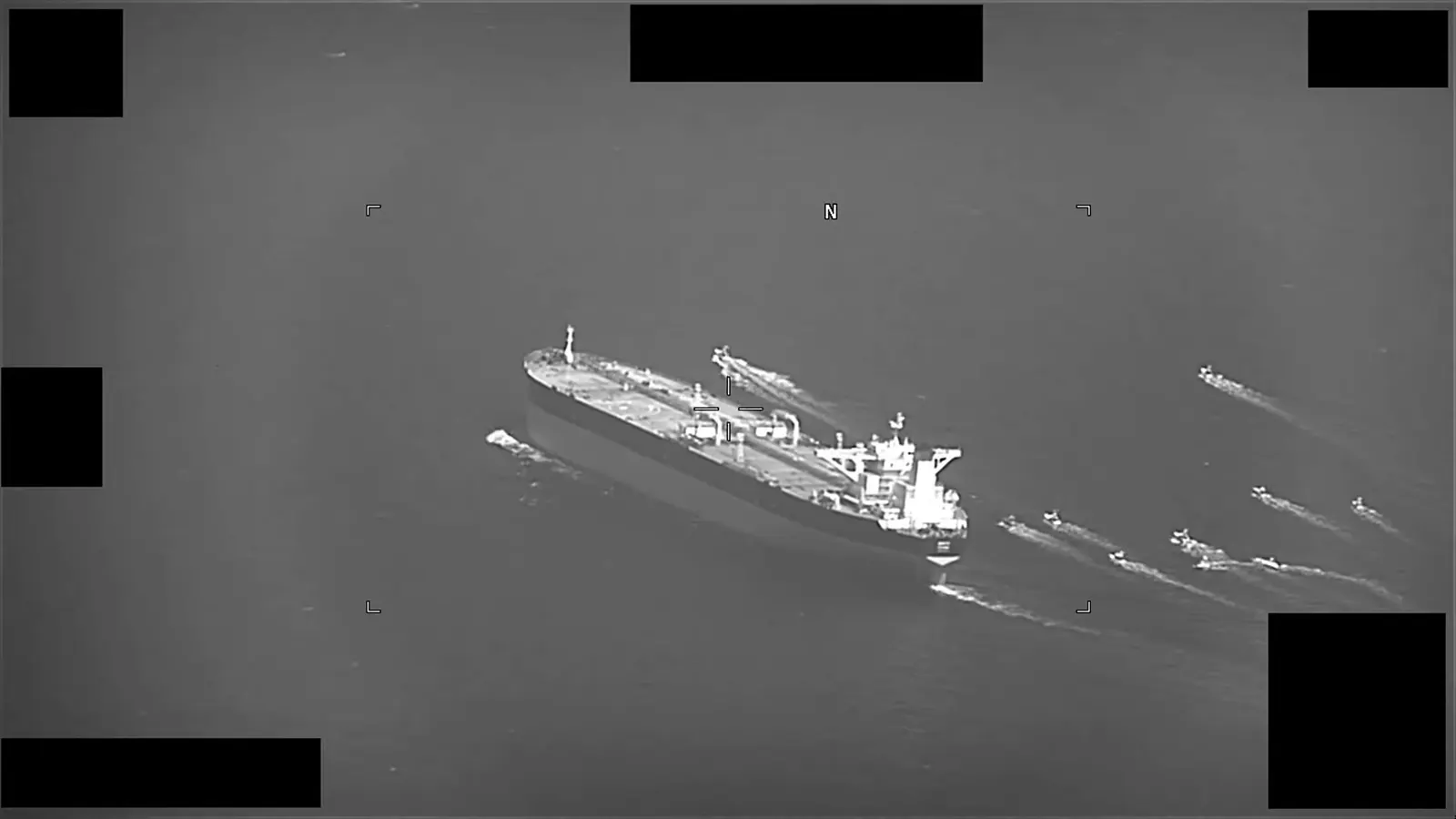 Imagen aérea en blanco y negro de un petrolero cargado navegando en mar abierto, rodeado por una decena de lanchas rápidas que dejan estelas a su popa y por su costado.