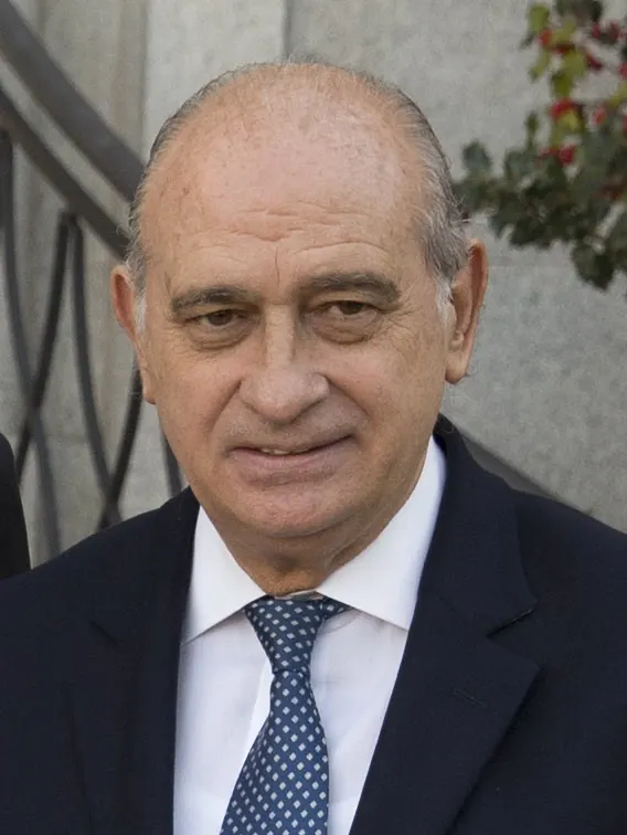 Retrato de Jorge Fernández Díaz, con traje azul oscuro, camisa blanca y corbata azul de topos, ante una pared de piedra clara.