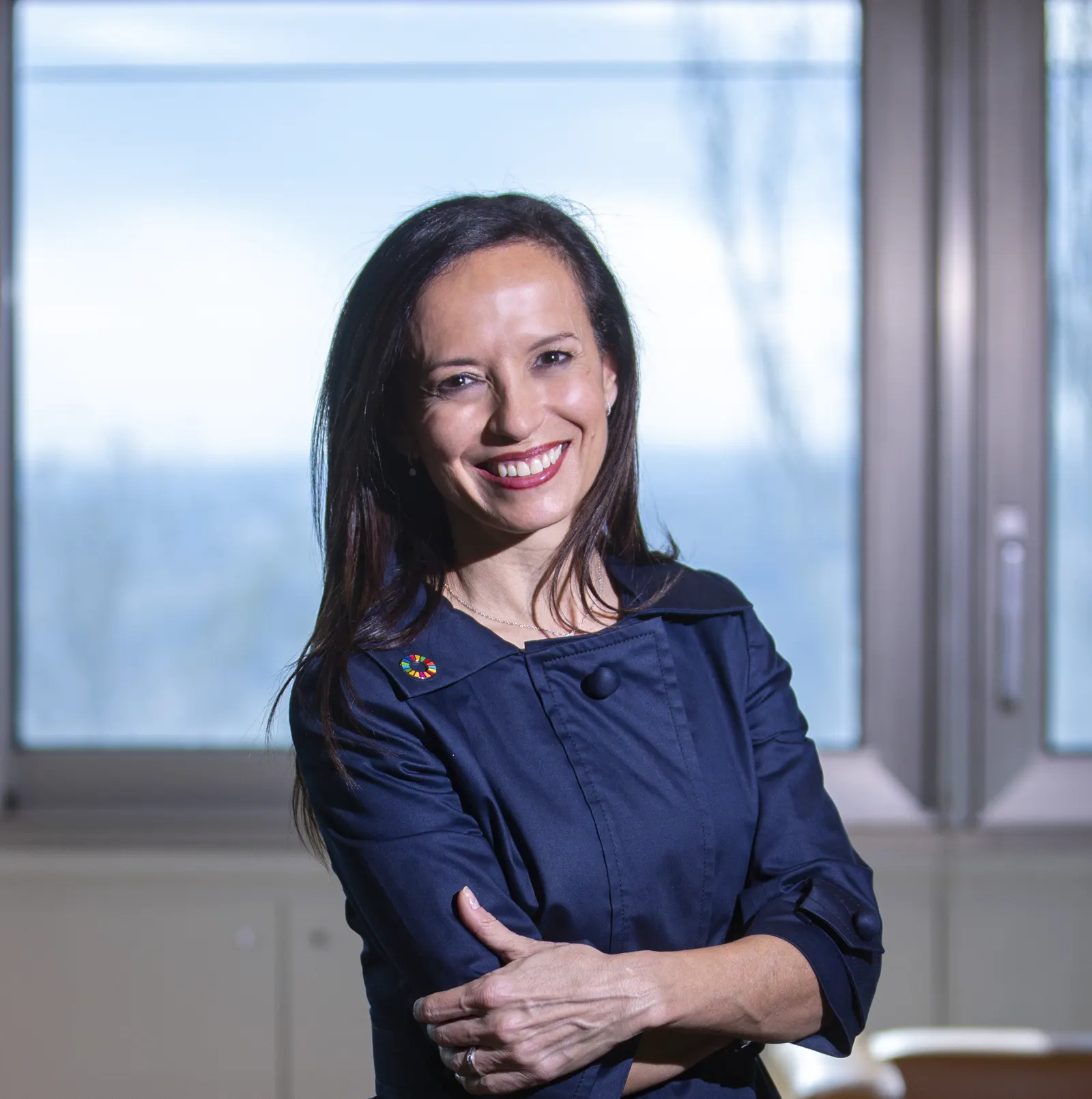 Retrato de Beatriz Corredor, presidenta de Redeia, sonriente y con los brazos cruzados ante un ventanal de una oficina