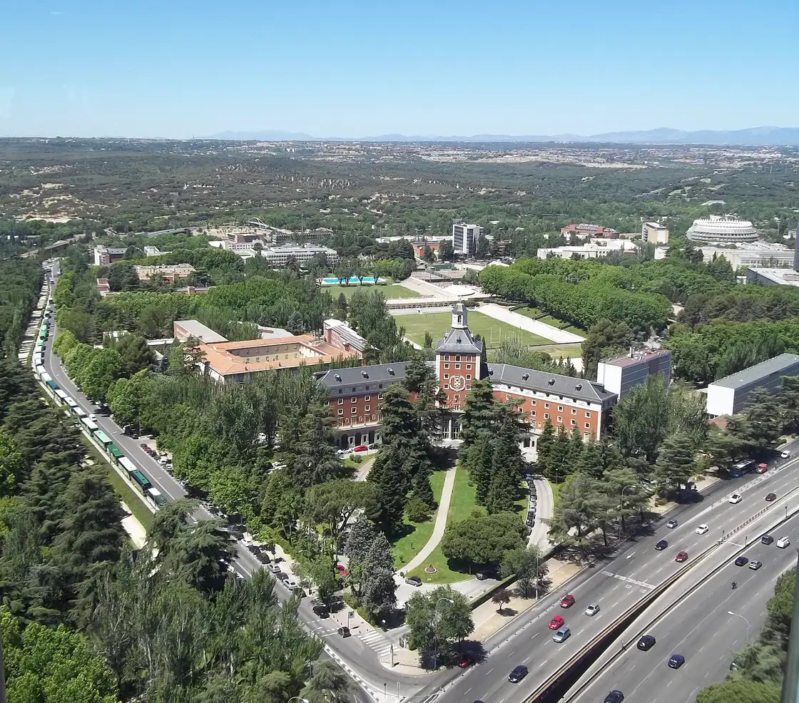 Vista aérea del rectorado de la Universidad Complutense de Madrid, edificio de ladrillo rojo con torre central, rodeado de arboledas en la Ciudad Universitaria
