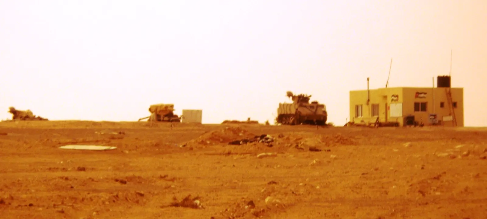 Vehículo blindado antiaéreo del Ejército jordano en el borde de una pista de tierra del desierto, junto a una caseta con banderas de Jordania.