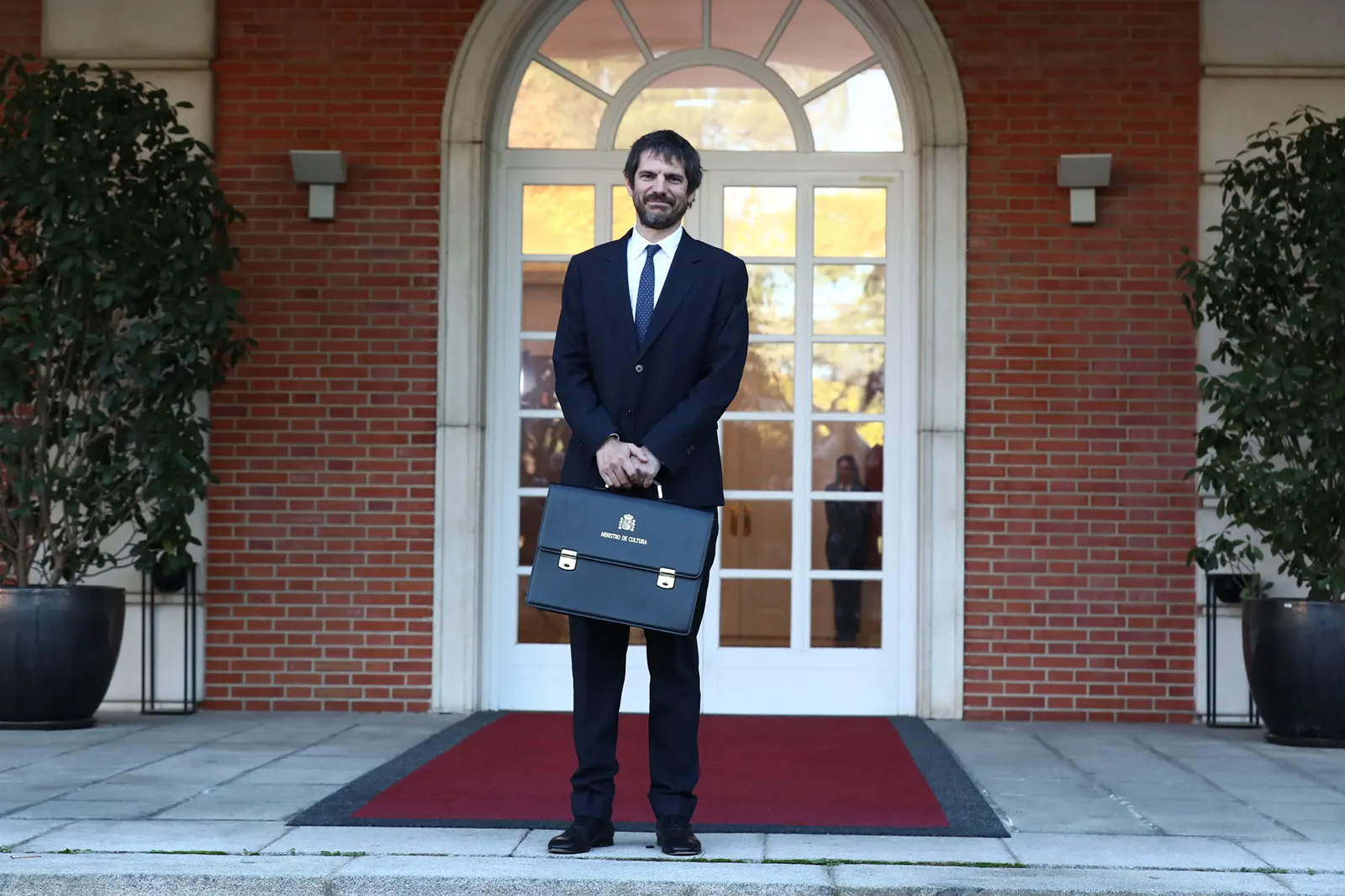 Ernest Urtasun, de traje oscuro y con una cartera de ministro en la mano, posa en la escalinata del complejo de La Moncloa