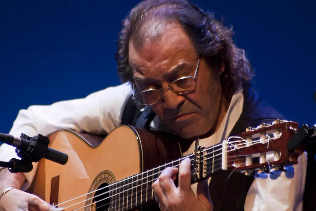 El guitarrista Pepe Habichuela, con gafas y camisa blanca, toca una guitarra flamenca ante un fondo azul