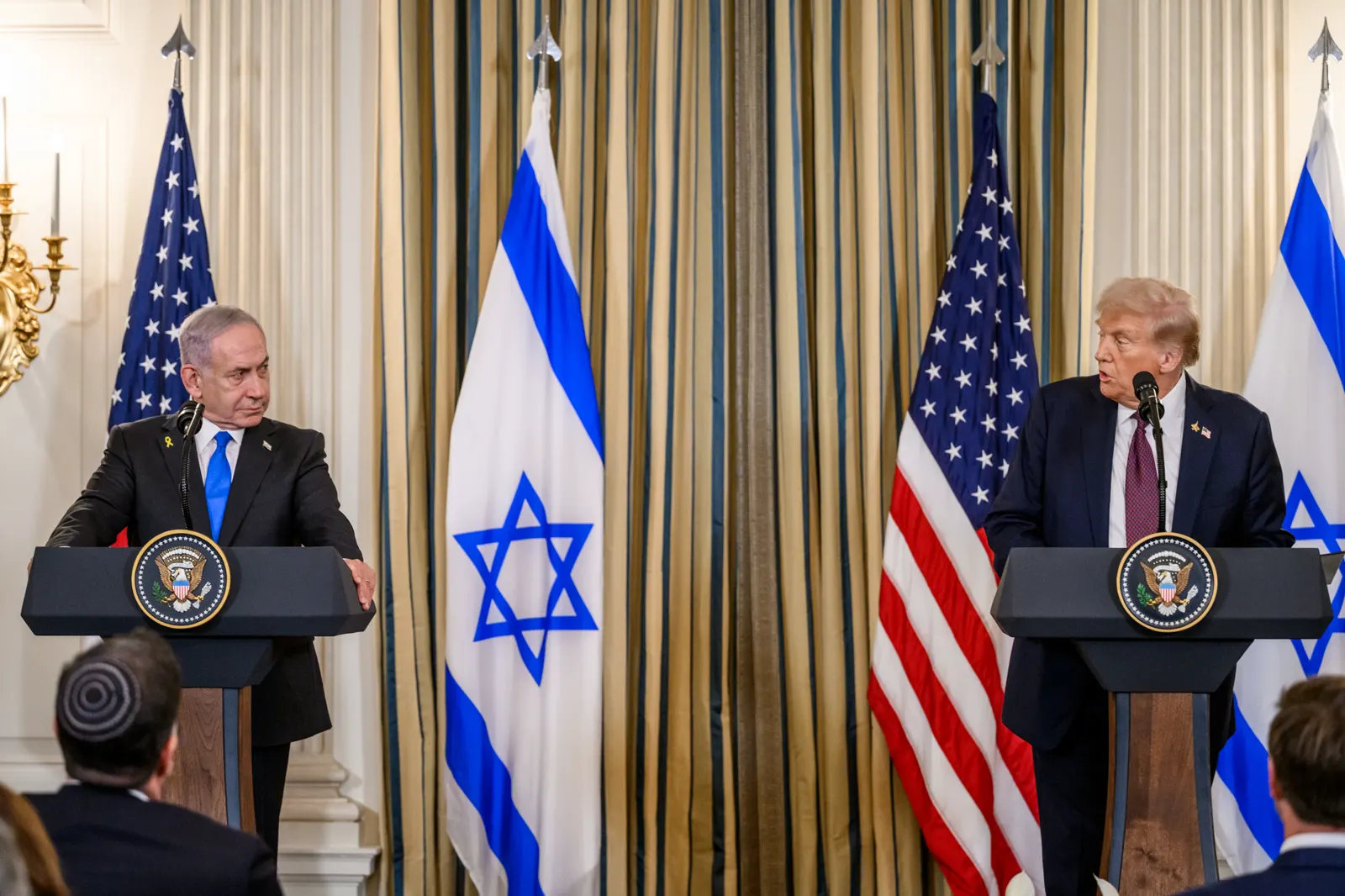 Benjamin Netanyahu y Donald Trump, cada uno tras un atril con el sello presidencial, frente a banderas de Estados Unidos e Israel en una sala de la Casa Blanca
