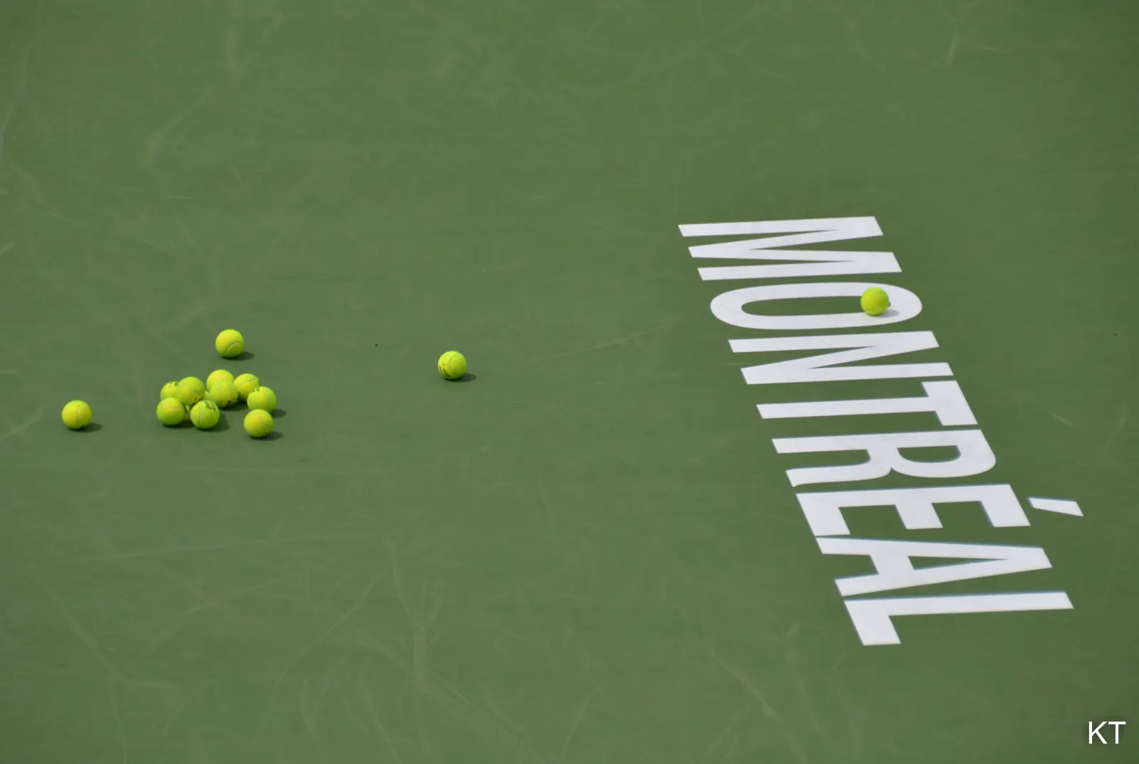 Pista de tenis de superficie dura verde vista desde arriba, con una decena de pelotas amarillas agrupadas a la izquierda y el rótulo blanco MONTRÉAL pintado sobre el suelo a la derecha.