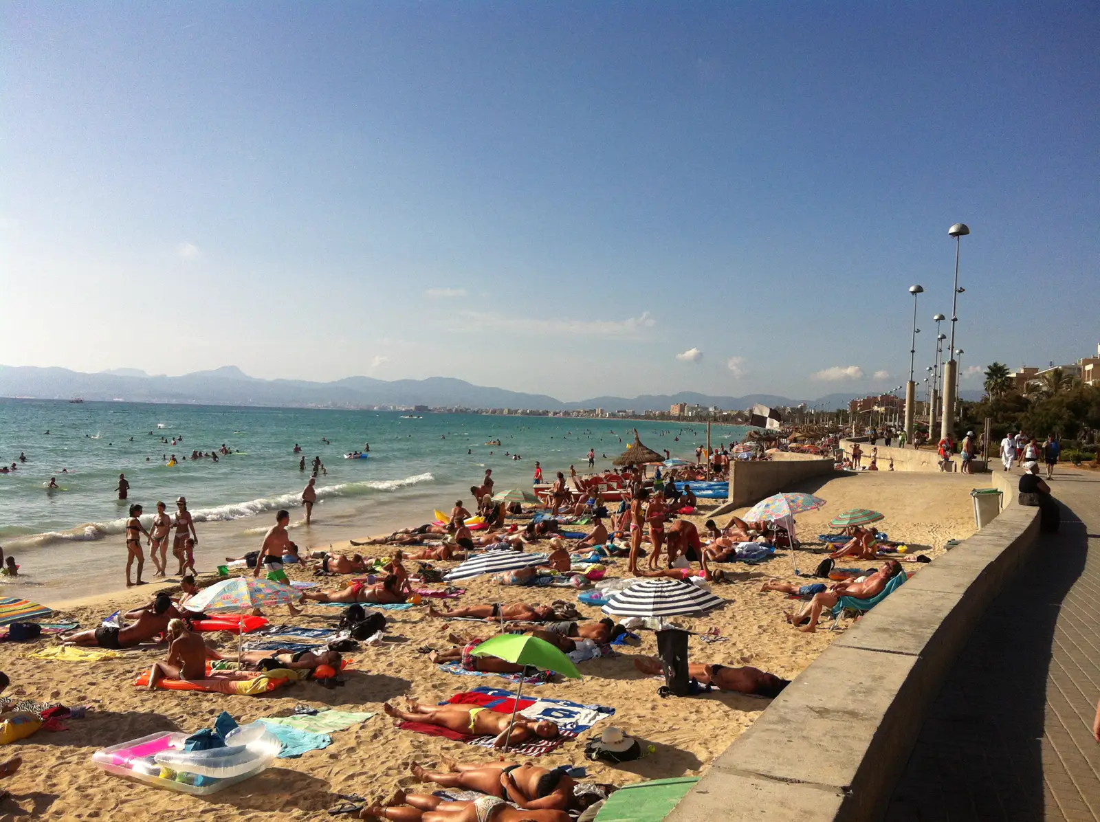 Bañistas con sombrillas y colchonetas sobre la arena de la playa de El Arenal, en Palma de Mallorca, con el mar y la bahía al fondo