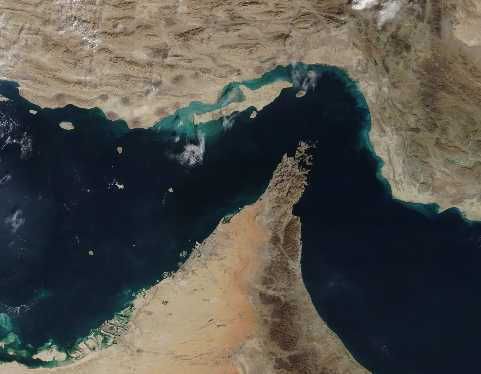 Imagen de satélite del estrecho de Ormuz: un brazo de mar azul oscuro separa la costa desértica de Irán, al norte, de la península de Musandam y el litoral árabe, al sur.