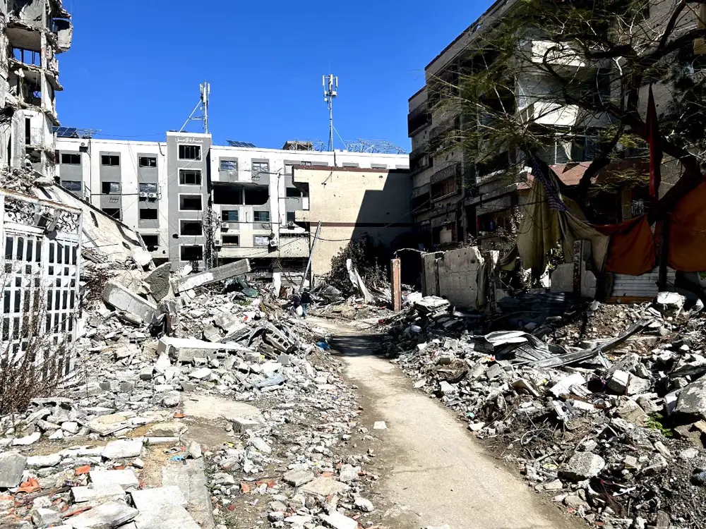 Callejón de tierra entre montañas de escombros de viviendas derruidas en la calle Al Wehda de Ciudad de Gaza, con edificios acribillados y sin ventanas al fondo bajo un cielo azul