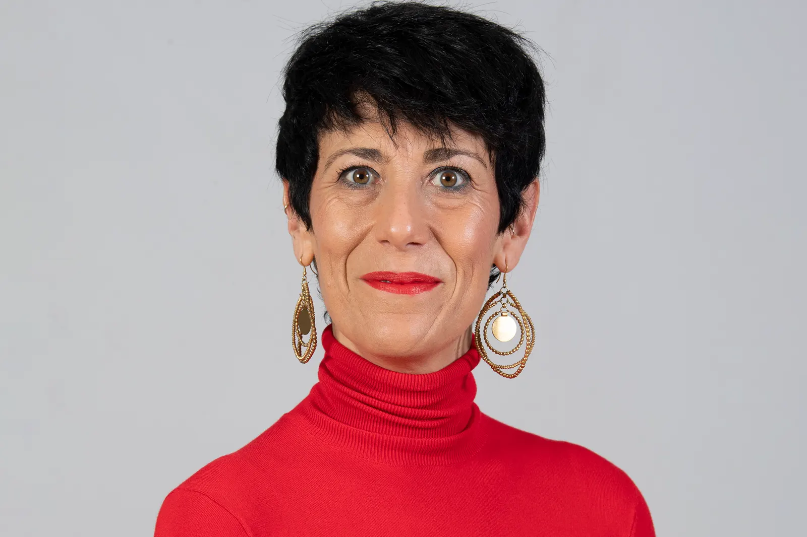 Retrato oficial de la ministra Elma Saiz, de pelo corto oscuro y jersey rojo de cuello alto, sobre fondo gris liso