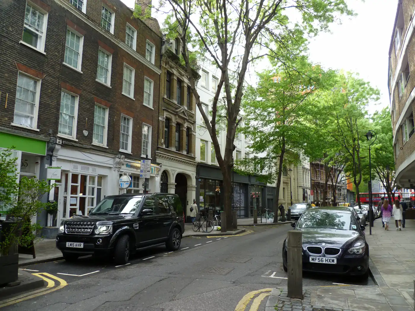 Vista de la calle Endell, en el barrio londinense de Covent Garden: una vía estrecha bordeada de edificios de ladrillo de varias plantas con tiendas en los bajos, coches aparcados junto al bordillo y árboles a ambos lados.