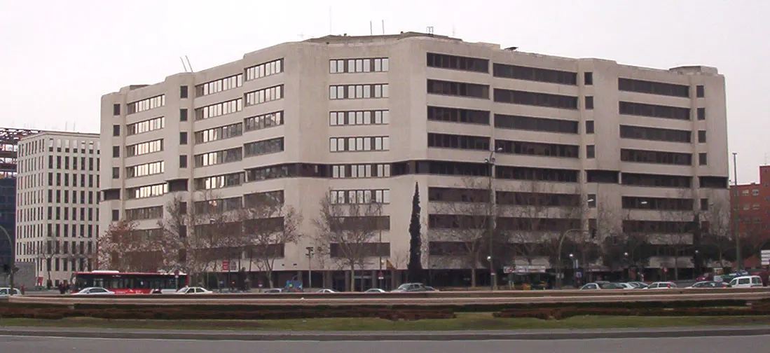 Edificio poligonal de hormigón claro de ocho plantas, sede de los juzgados de la plaza de Castilla de Madrid, con árboles sin hojas y coches en primer término