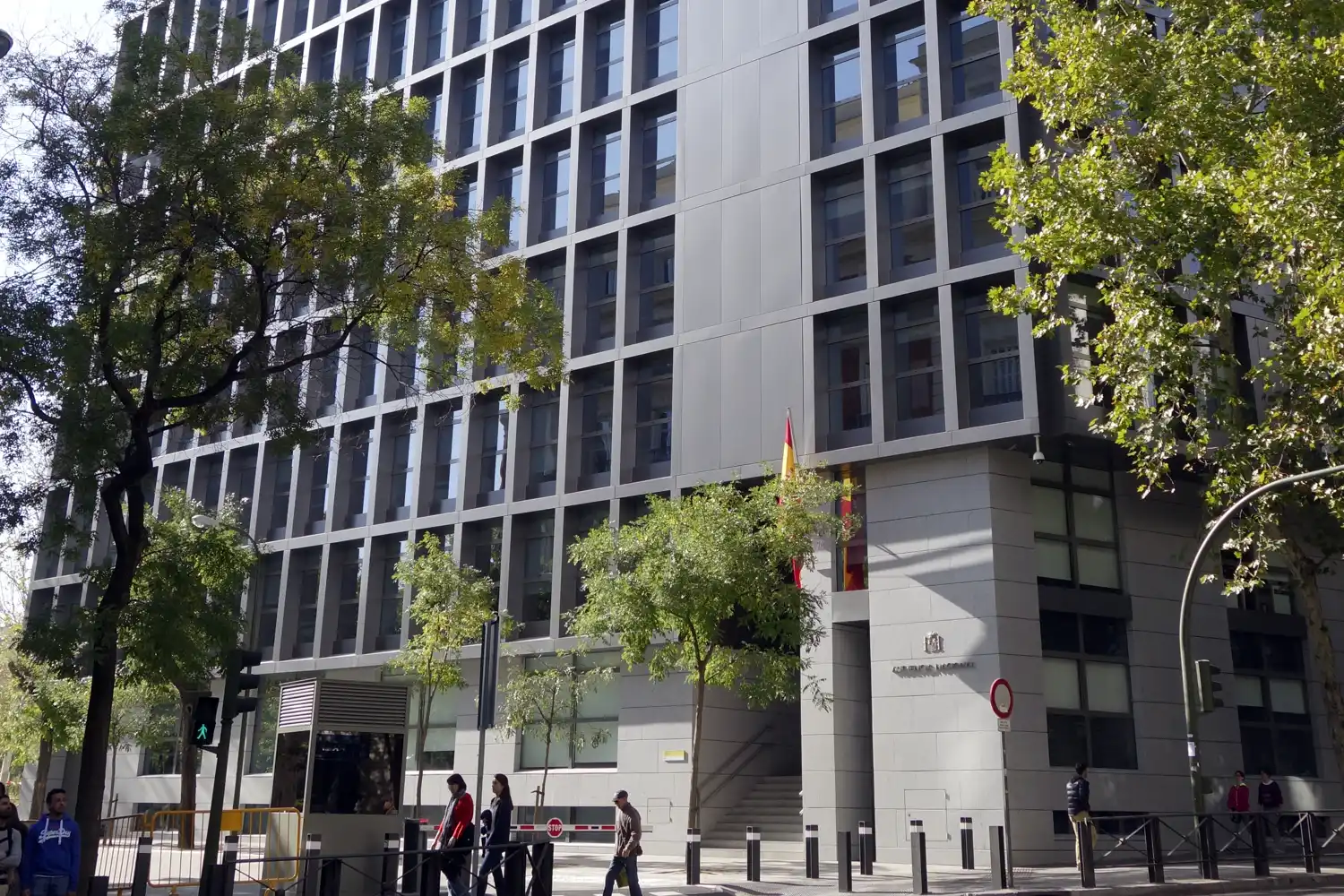 Fachada del edificio de la Audiencia Nacional en Madrid, con una bandera de España sobre la entrada principal y viandantes en la acera.