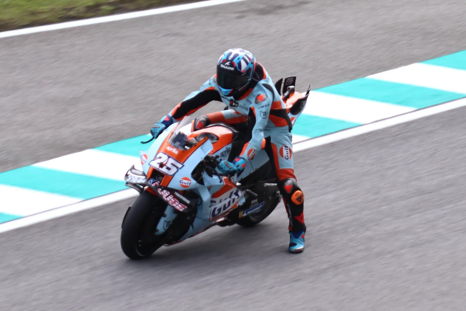 Raúl Fernández, con mono azul y naranja, inclina su moto número 25 del equipo Trackhouse al tomar una curva de un circuito.