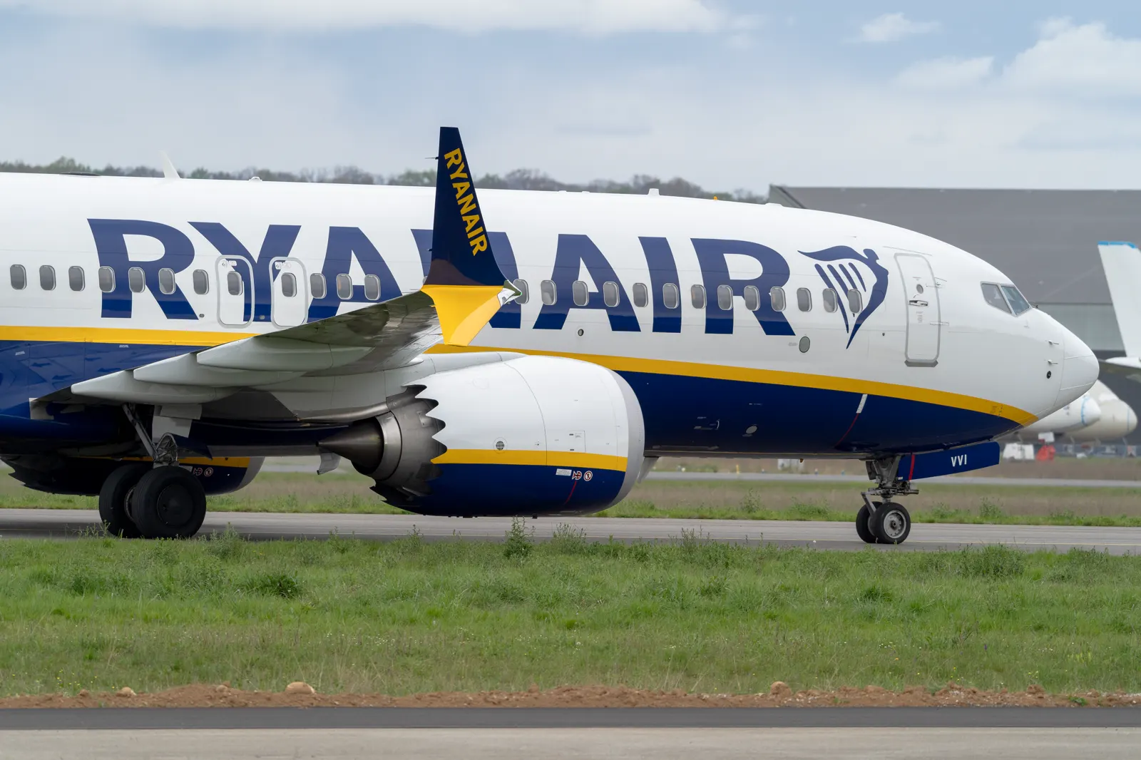 Un Boeing 737 con la librea blanca, azul y amarilla de Ryanair rueda por la pista de un aeropuerto, con el arpa del logotipo pintada en el morro.