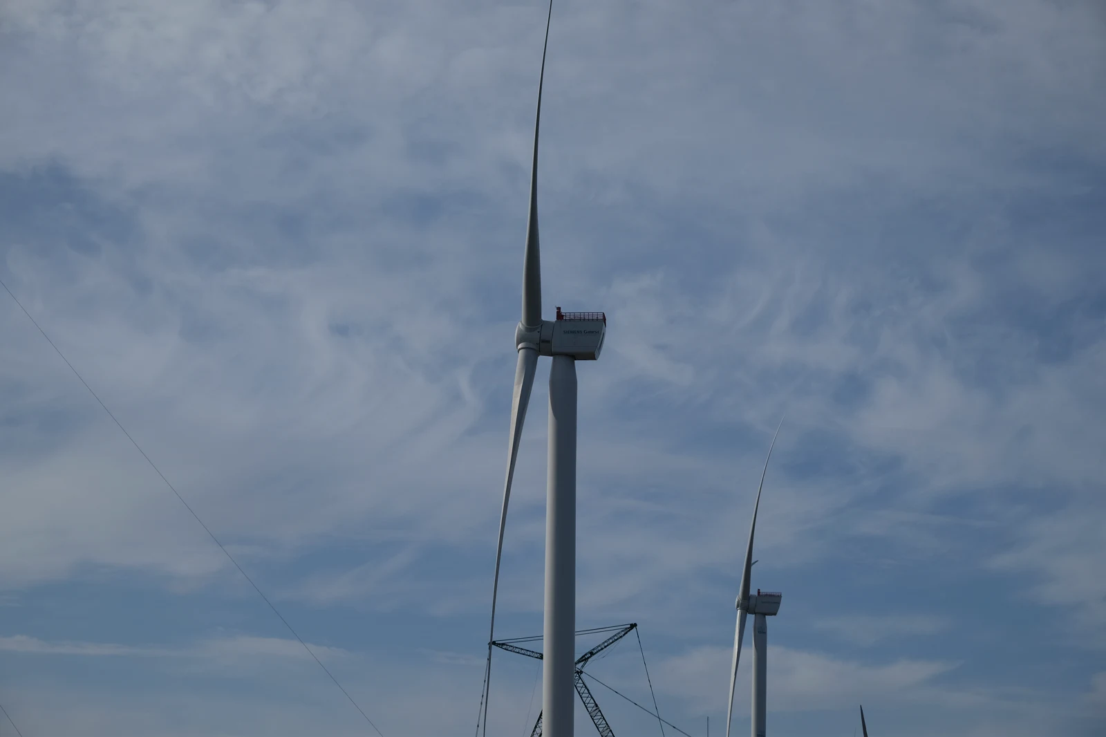 Dos aerogeneradores de Siemens Gamesa recortados contra un cielo nublado; en la góndola del más cercano se lee el logotipo de la marca.