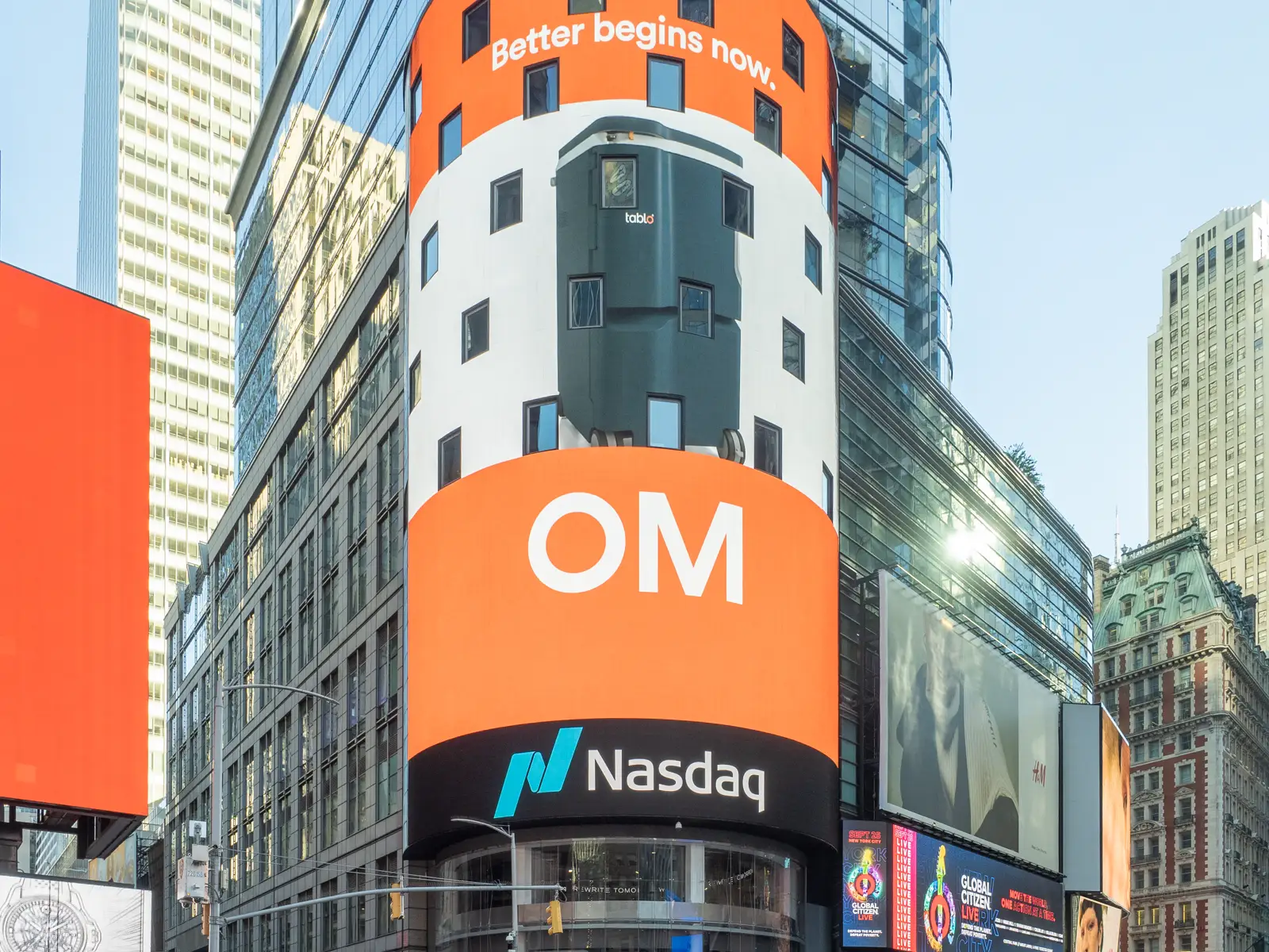 Torre acristalada de la sede del Nasdaq en Times Square, con una gran pantalla curva naranja y el logotipo del mercado bajo ella, rodeada de rascacielos y vallas publicitarias.