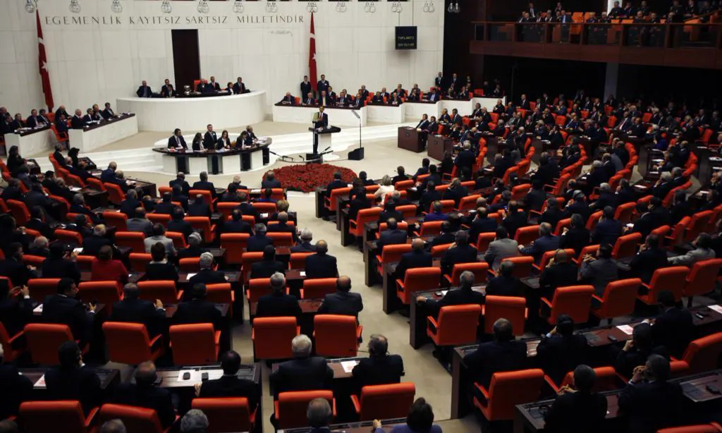Hemiciclo de la Gran Asamblea Nacional de Turquía, con los escaños rojos ocupados por diputados y el lema «La soberanía pertenece incondicionalmente a la nación» en el muro del fondo.