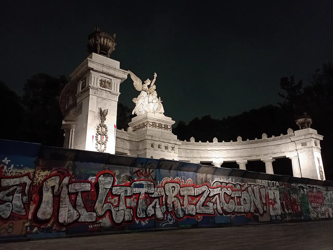 Vallas metálicas cubiertas de pintadas protegen de noche el Hemiciclo a Juárez, monumento de mármol blanco iluminado en Ciudad de México