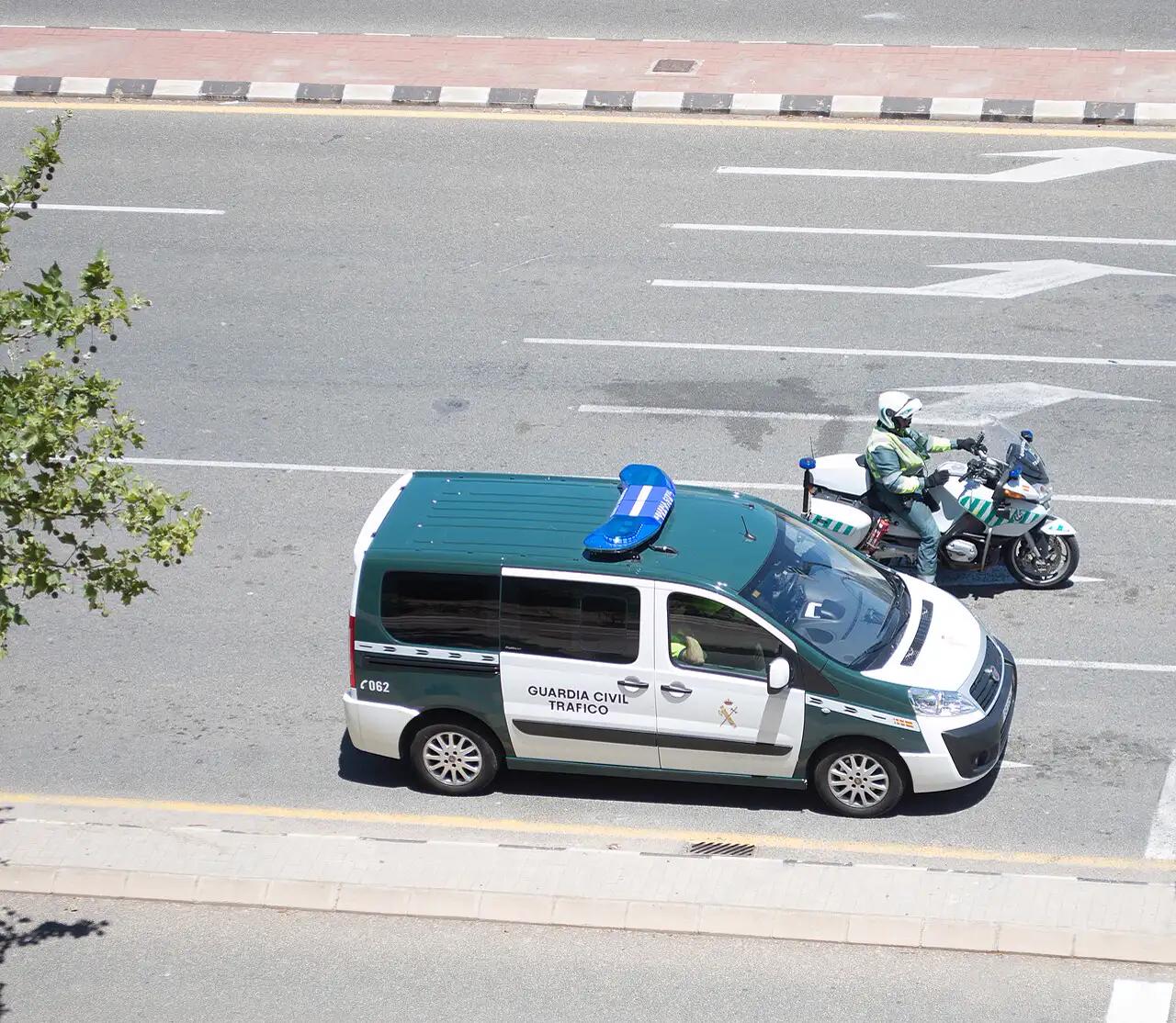 Furgoneta verde y blanca con el rótulo «Guardia Civil Tráfico» y un motorista de la misma unidad, con casco y chaleco reflectante, detenidos en una calzada urbana vistos desde arriba