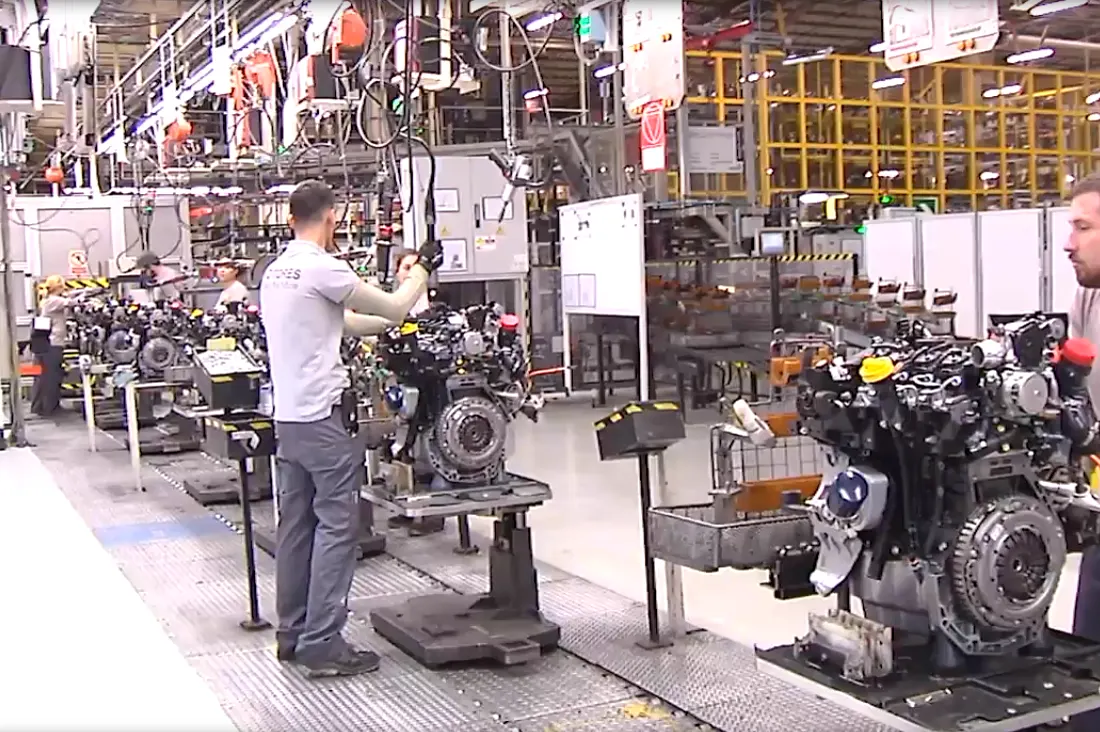 Operarios montan motores de automóvil sobre soportes metálicos en una línea de producción de la factoría de Renault en Valladolid, con estructuras y utillaje industrial al fondo.