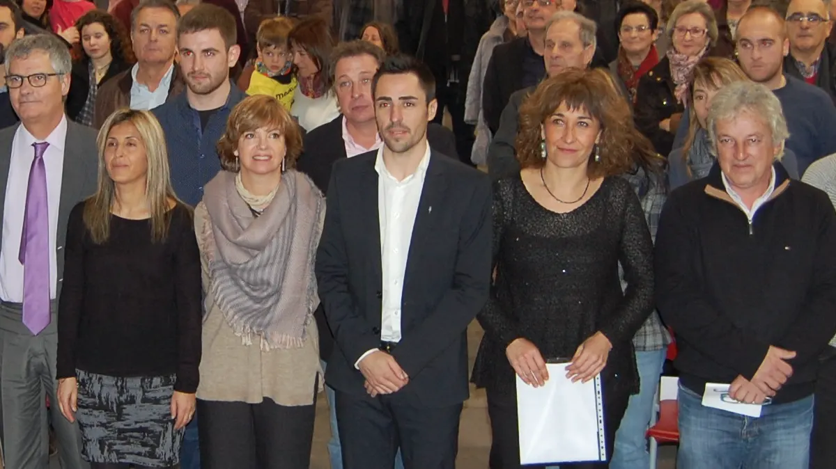 Fila de asistentes a un acto institucional en una sala; en el centro, un hombre joven con traje oscuro y camisa blanca, Marc Puigtió