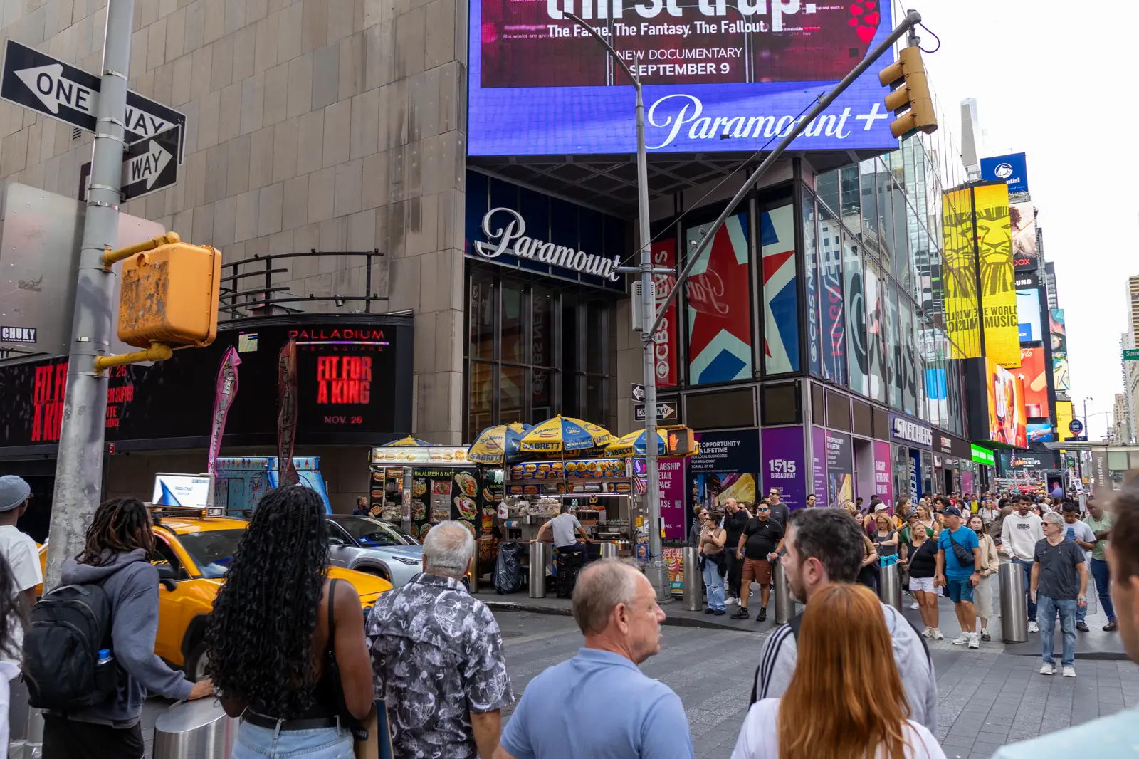Esquina de One Astor Plaza, en Times Square (Nueva York), con el rótulo Paramount sobre la entrada, una pantalla publicitaria de Paramount+ encima y peatones y un taxi amarillo en primer plano