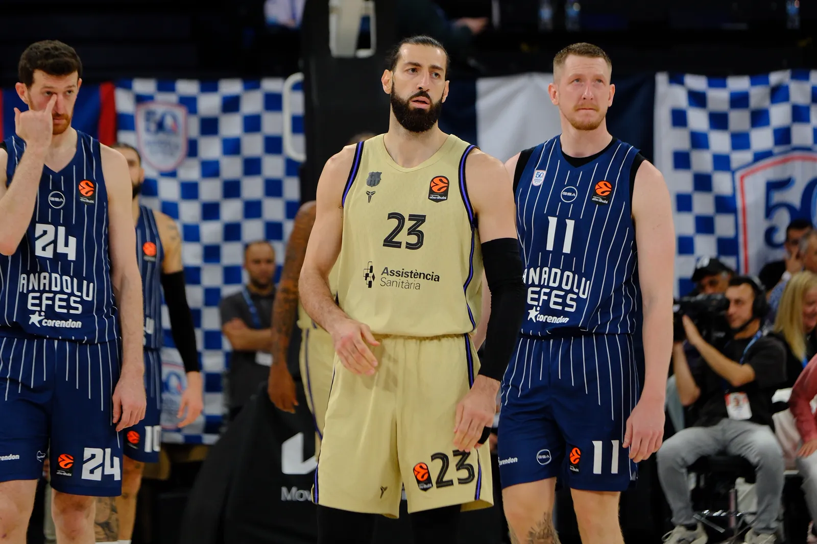 Tornike Shengelia, con la camiseta dorada número 23 del FC Barcelona, camina por la pista entre dos jugadores del Anadolu Efes con equipación azul a rayas, durante un partido de Euroliga.