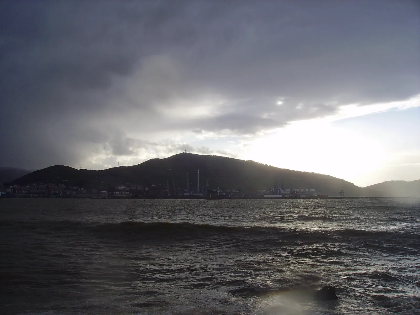 Nubes de tormenta bajas y oscuras sobre el monte Serantes y el puerto de Bizkaia, con la desembocadura del Nervión en primer plano y el mar picado.