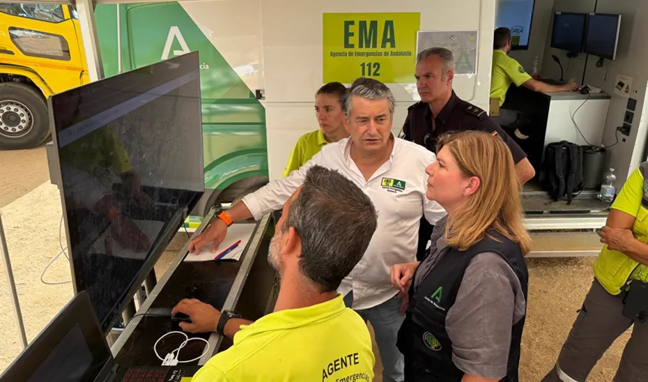 Media docena de personas, varias con el polo amarillo de la Agencia de Emergencias de Andalucía, observan dos pantallas dentro del puesto de mando avanzado montado junto a un vehículo con el rótulo «EMA 112».