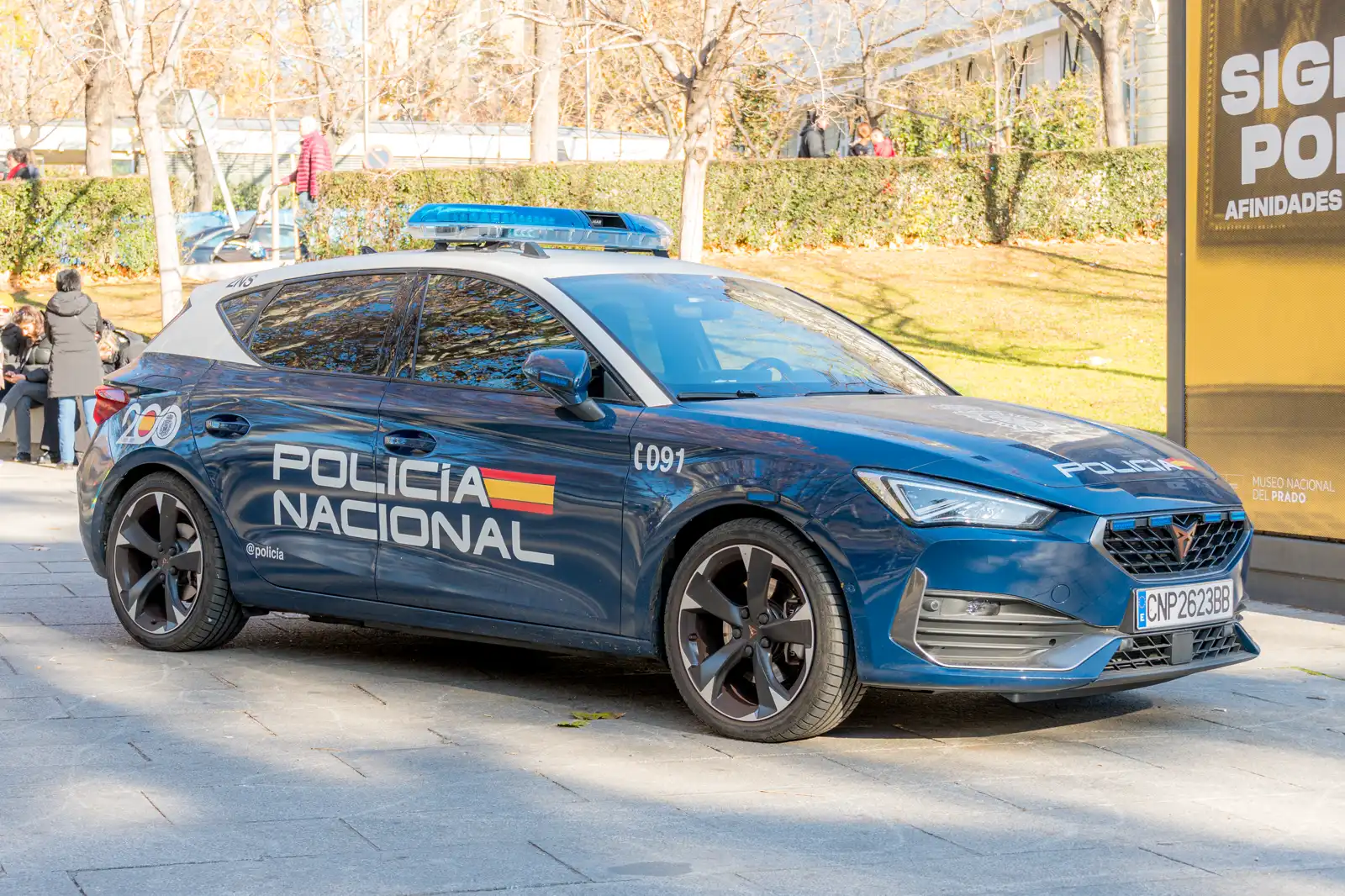 Coche patrulla azul de la Policía Nacional española, con el rótulo «Policía Nacional» y el número 091 en la carrocería, estacionado en una acera arbolada de Madrid.