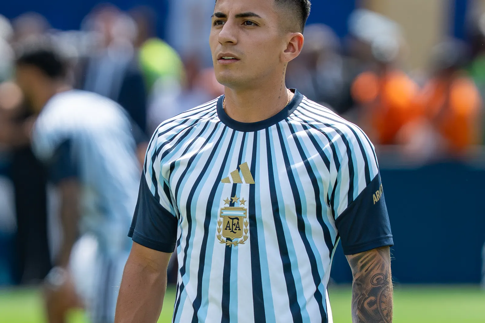 El futbolista Thiago Almada, con la camiseta a rayas blancas y celestes de la selección argentina, de pie sobre el césped de un estadio.