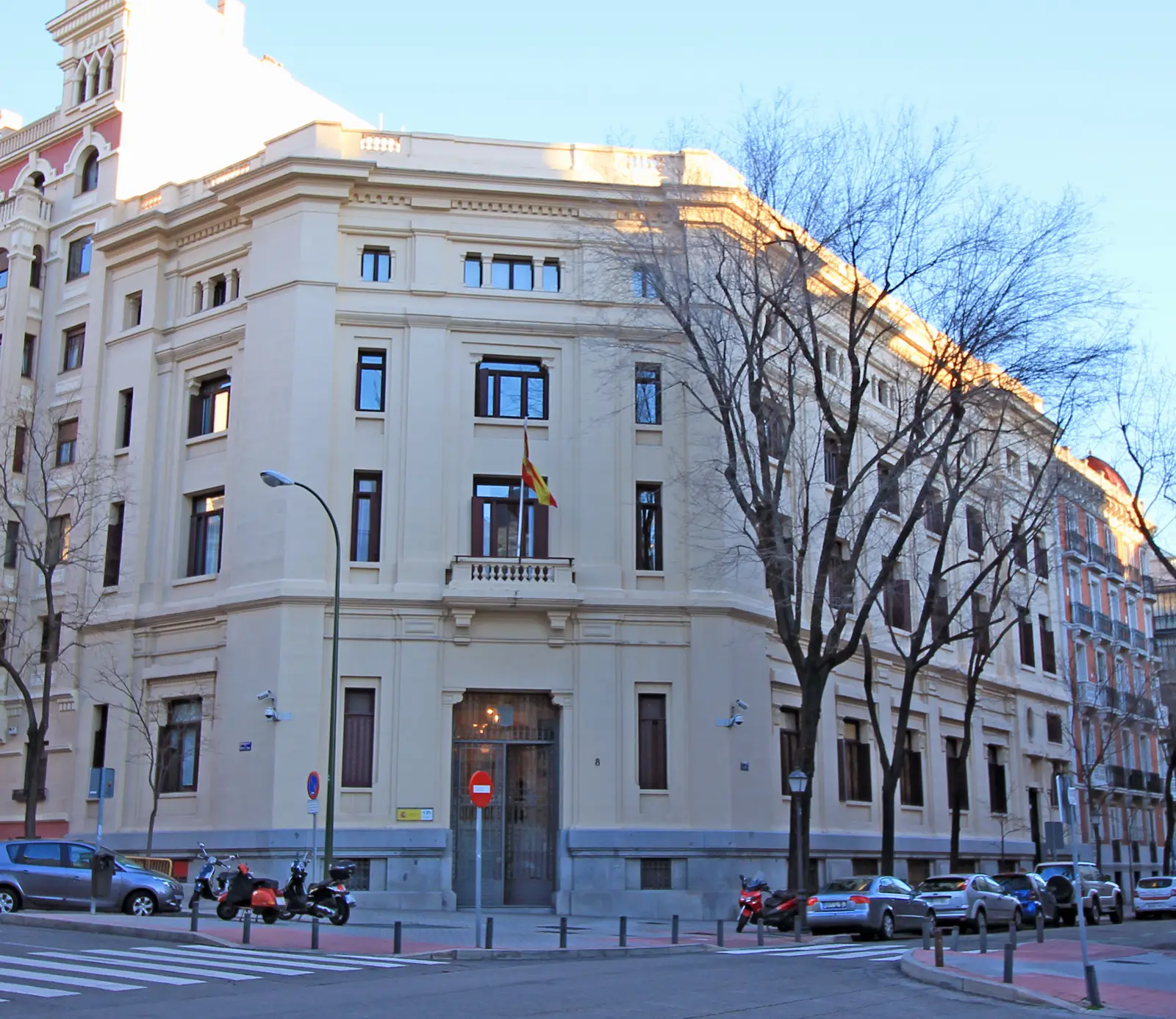 Fachada en esquina de un edificio institucional de piedra clara con bandera de España sobre la puerta, sede del Centro de Investigaciones Sociológicas en el número 8 de la calle Montalbán de Madrid.