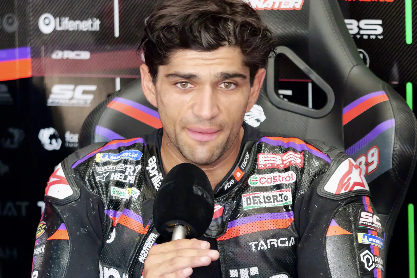 Jorge Martín, con el mono de cuero de Aprilia y el dorsal 89, sentado en el box y hablando ante un micrófono.