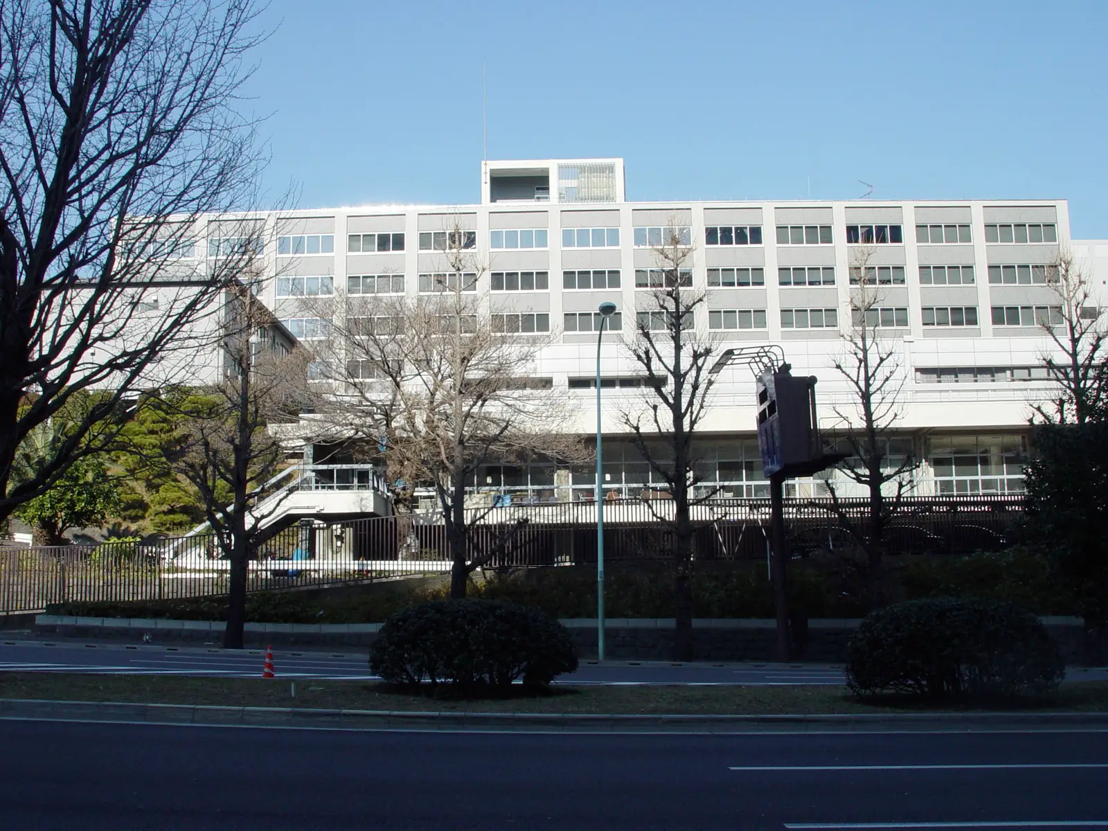 Edificio blanco de seis plantas de la Oficina del Gabinete del Gobierno de Japón, visto desde la acera de enfrente entre árboles sin hojas, en el barrio de Nagatacho de Tokio.