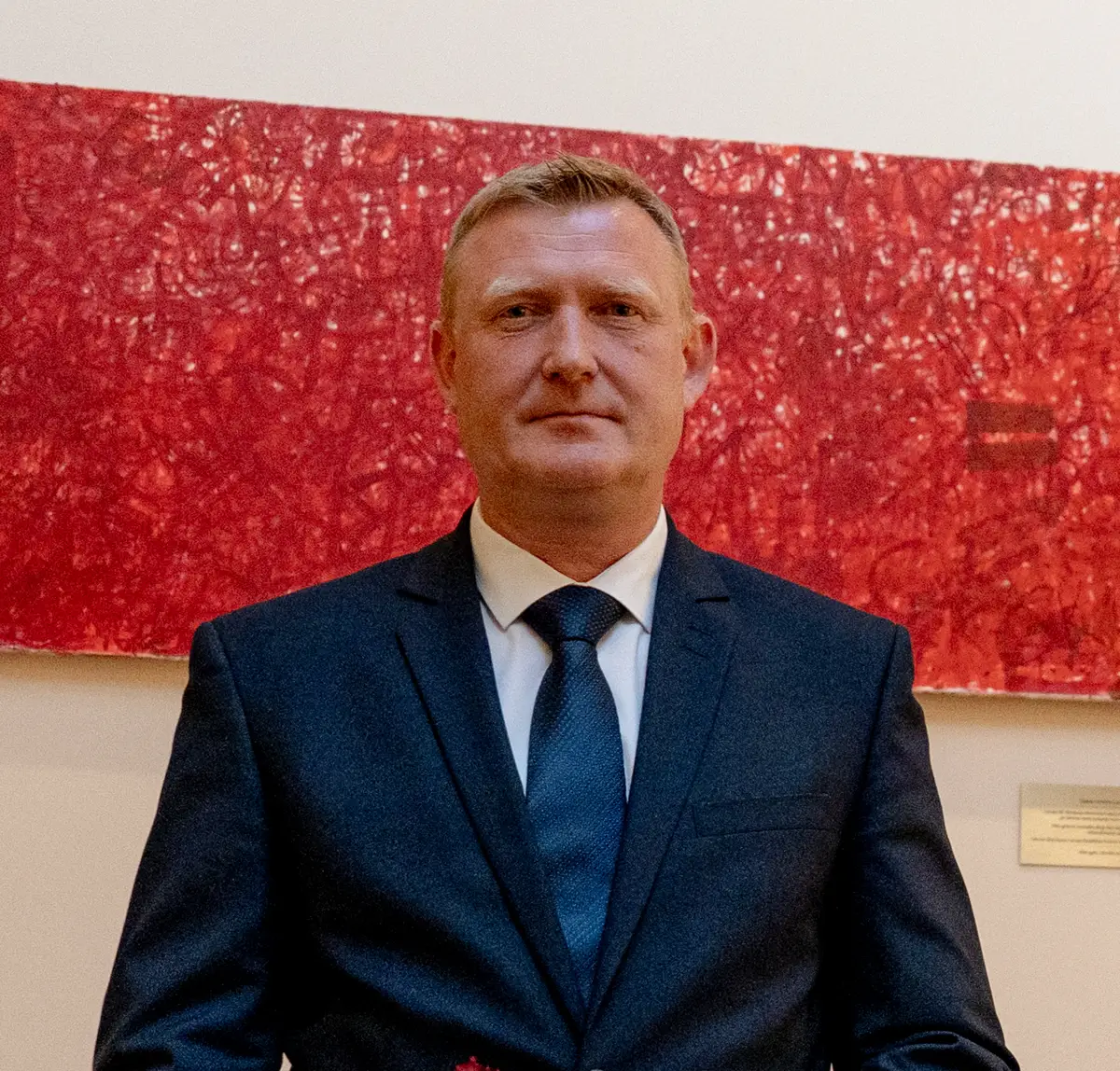 Raivis Melnis, ministro de Defensa de Letonia, de traje oscuro y corbata azul, ante un cuadro rojo en el Parlamento letón