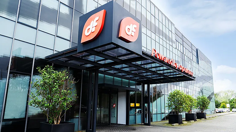 Fachada acristalada de la sede corporativa de Duro Felguera, con una marquesina de entrada rematada por dos logotipos rojos con las letras «df» y el lema «Powered by experience» rotulado en el cristal.