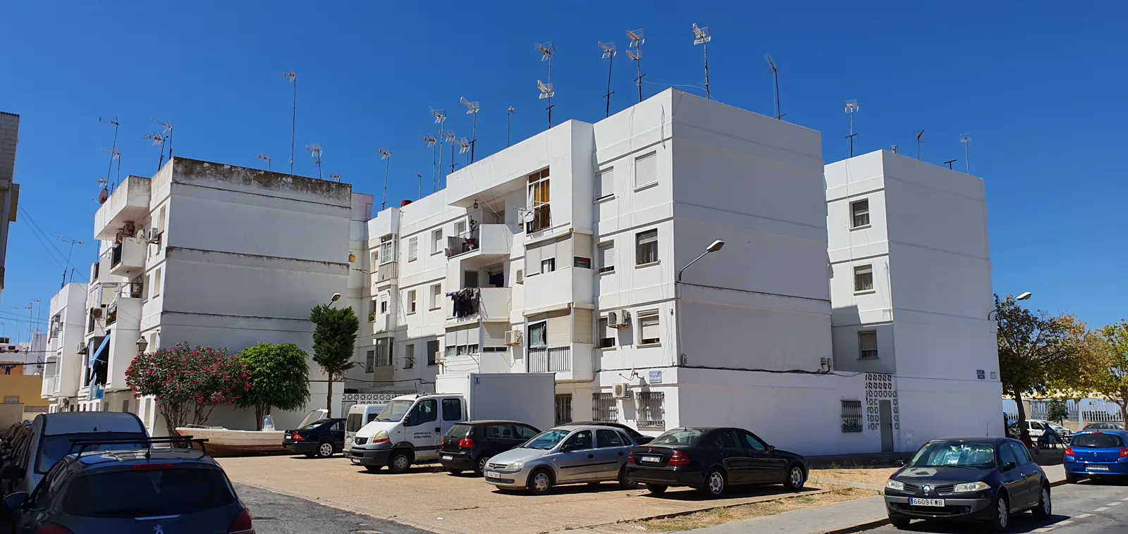 Bloques de viviendas blancos de tres alturas junto a una explanada con coches aparcados, en Isla Cristina (Huelva)
