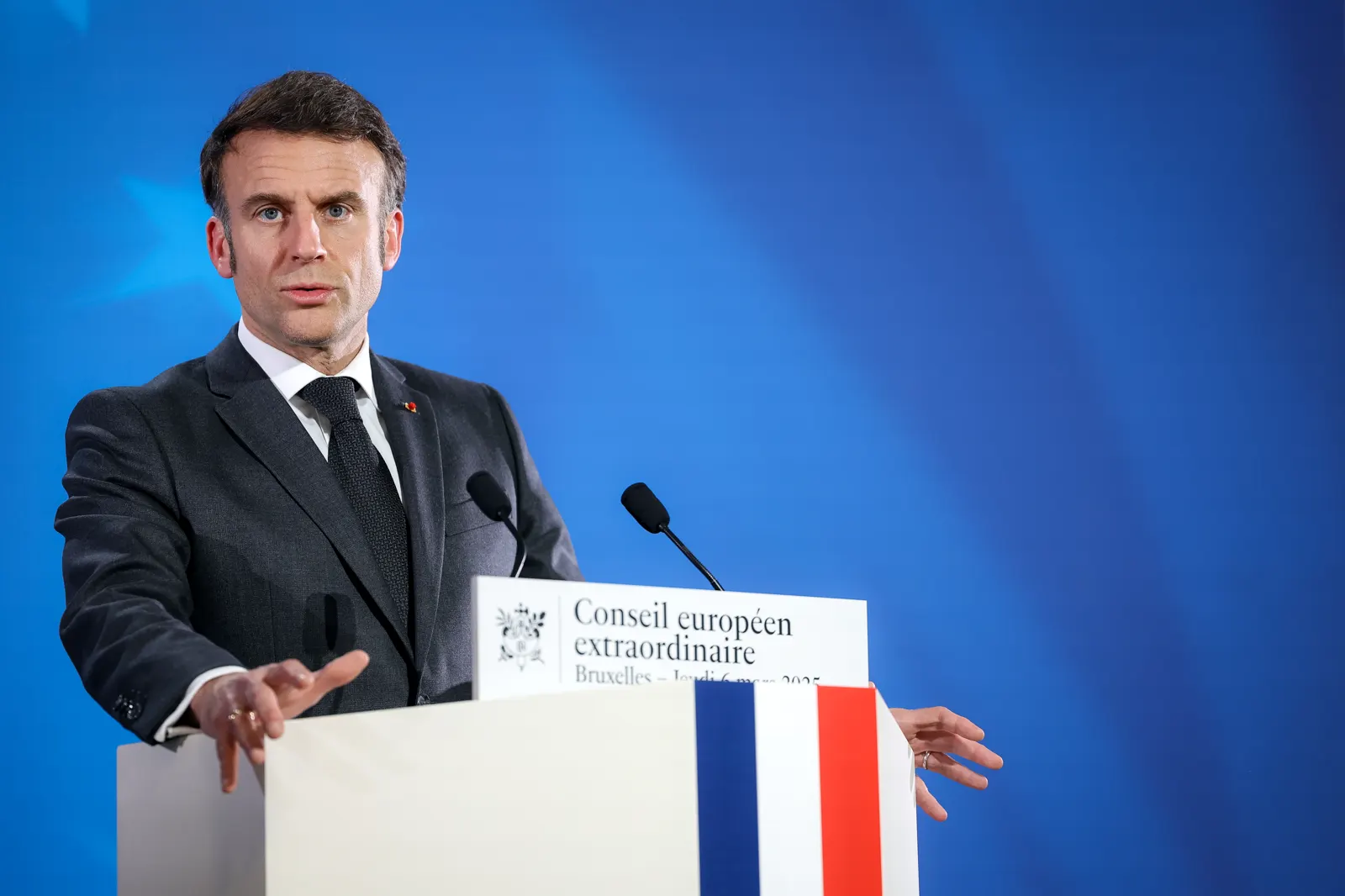 Emmanuel Macron, de traje oscuro, habla con las manos apoyadas en un atril rotulado «Conseil européen extraordinaire, Bruxelles», ante un fondo azul