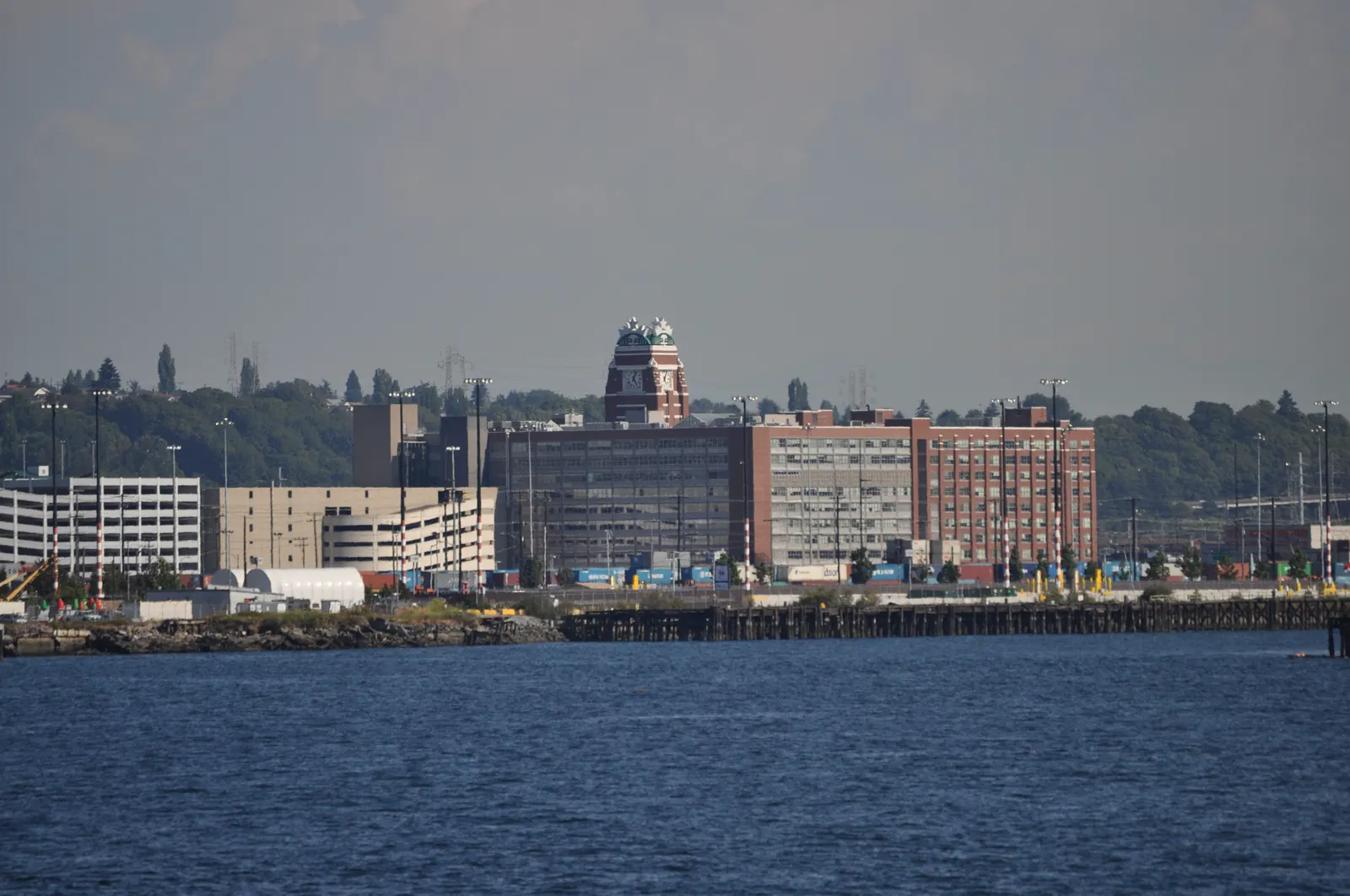 Vista desde el agua del Starbucks Center de Seattle: un edificio de ladrillo rojo de varias plantas rematado por una torre con el logotipo verde de la sirena de Starbucks, con la bahía en primer plano.