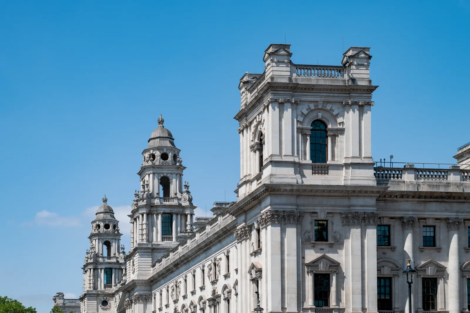 Fachada de piedra clara del edificio del Tesoro británico en Whitehall, Londres, con sus torreones y columnas recortados contra un cielo azul.