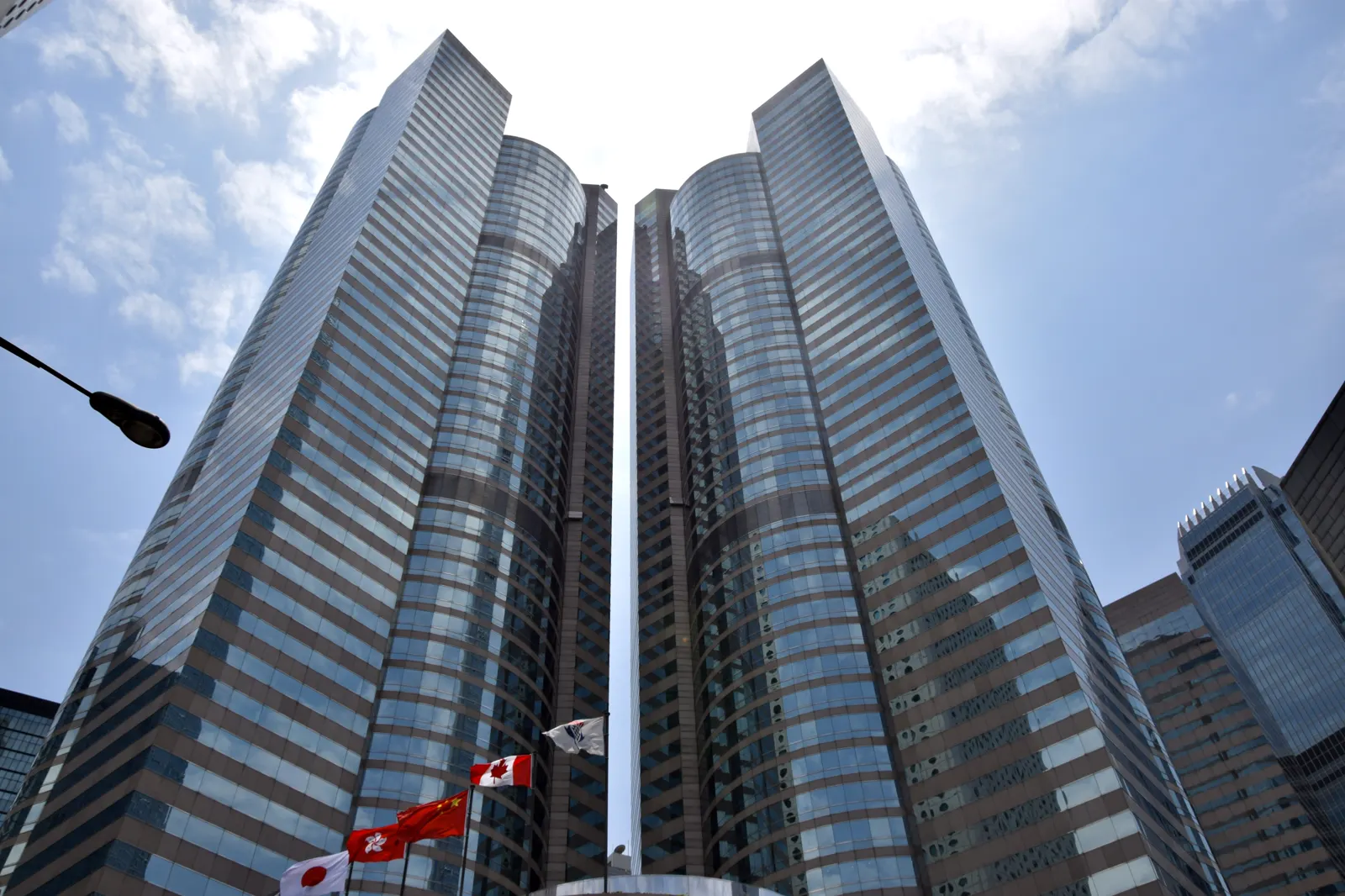 Las dos torres acristaladas de Exchange Square, en el distrito Central de Hong Kong, fotografiadas desde la calle en contrapicado, con banderas ondeando al pie.