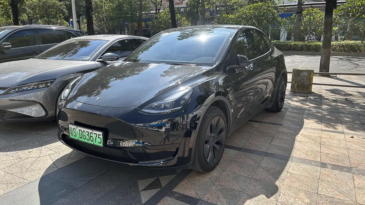 Tesla Model Y negro aparcado en una acera de Dongguan (China), con matrícula verde de vehículo eléctrico y otro coche a su izquierda