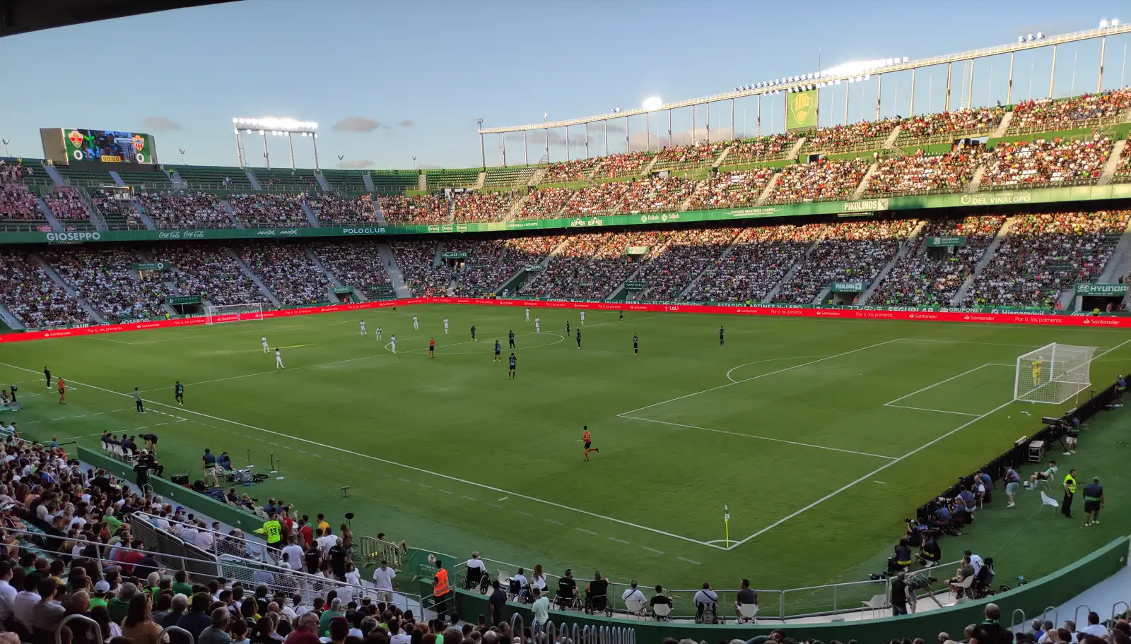 Vista general del interior del estadio Martínez Valero de Elche durante un partido, con el césped en primer plano, jugadores repartidos por el campo y las gradas llenas al fondo
