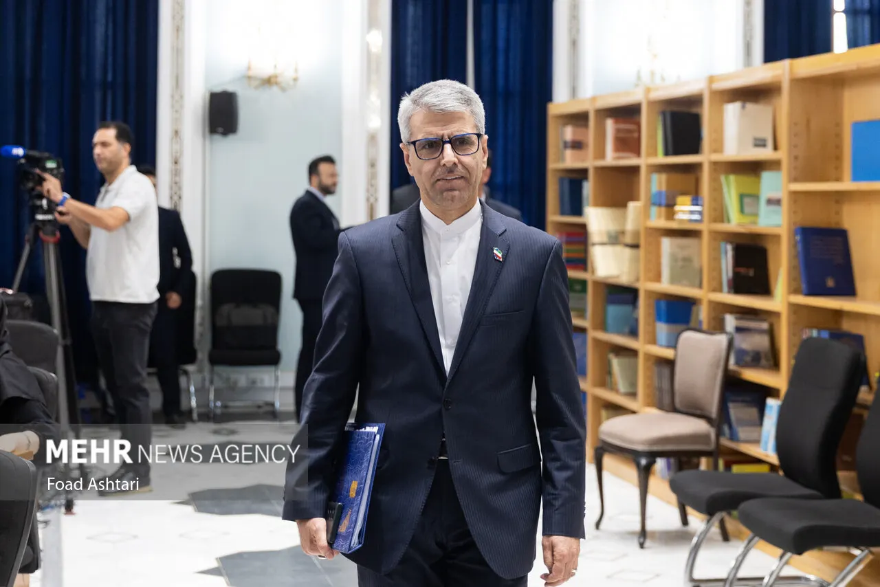 Esmaeil Baqaei, portavoz del Ministerio de Exteriores de Irán, camina con una carpeta bajo el brazo en una sala con estanterías de libros, ante cámaras de televisión