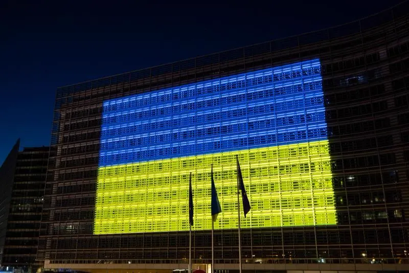 Fachada del edificio Berlaymont, sede de la Comisión Europea en Bruselas, iluminada de noche con los colores azul y amarillo de la bandera de Ucrania